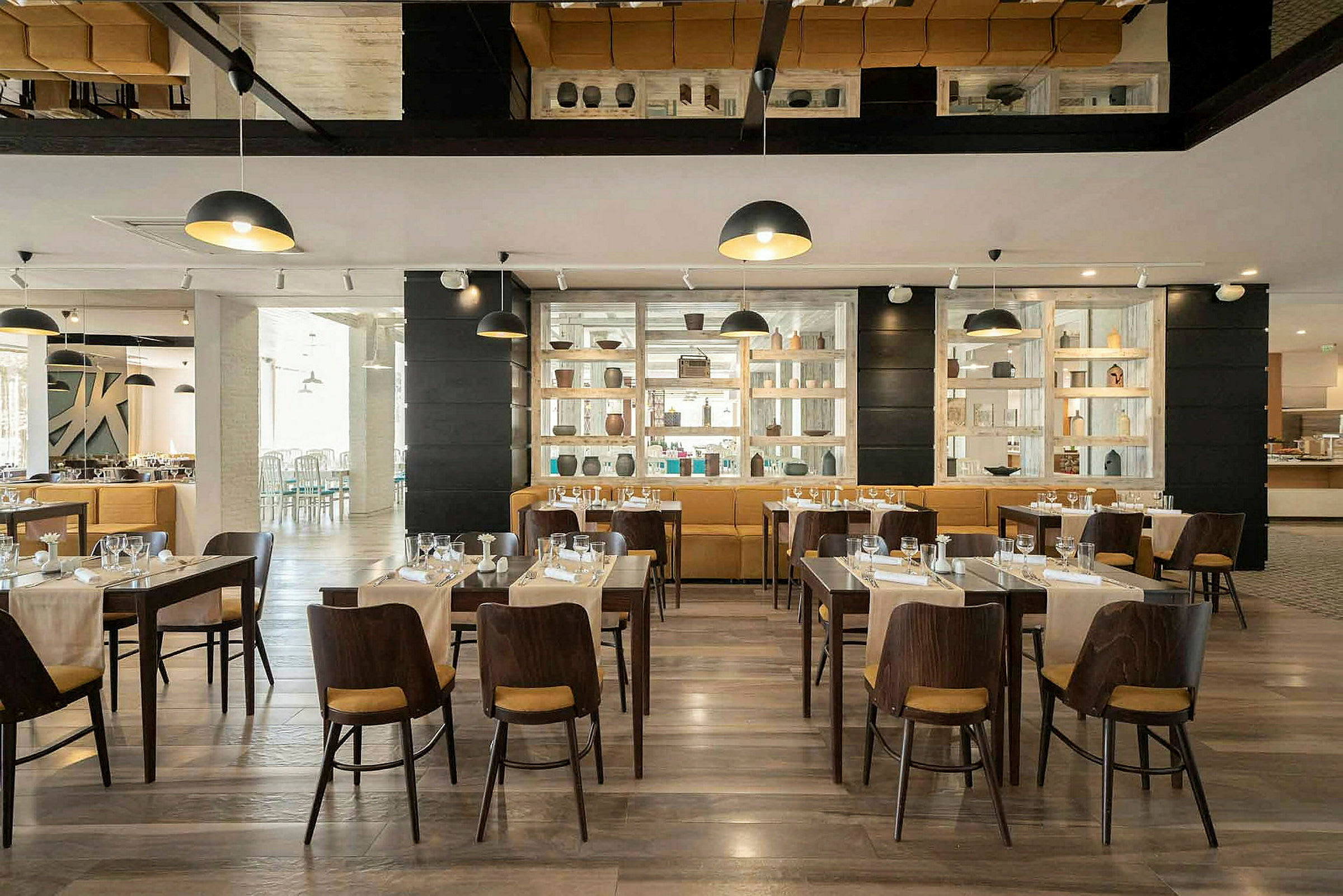 En restaurang med dukade träbord och stolar. Dekorativ hylla vid väggen. (AI-genererad text)
