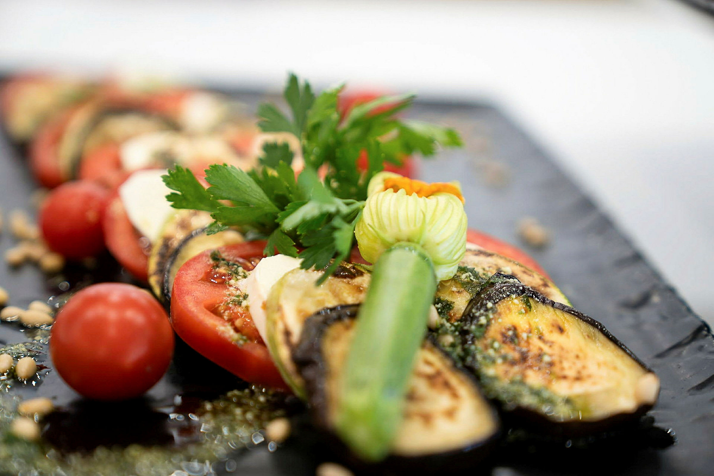 En tallrik med rostad aubergine, tomat, och färska örter. (AI-genererad text)