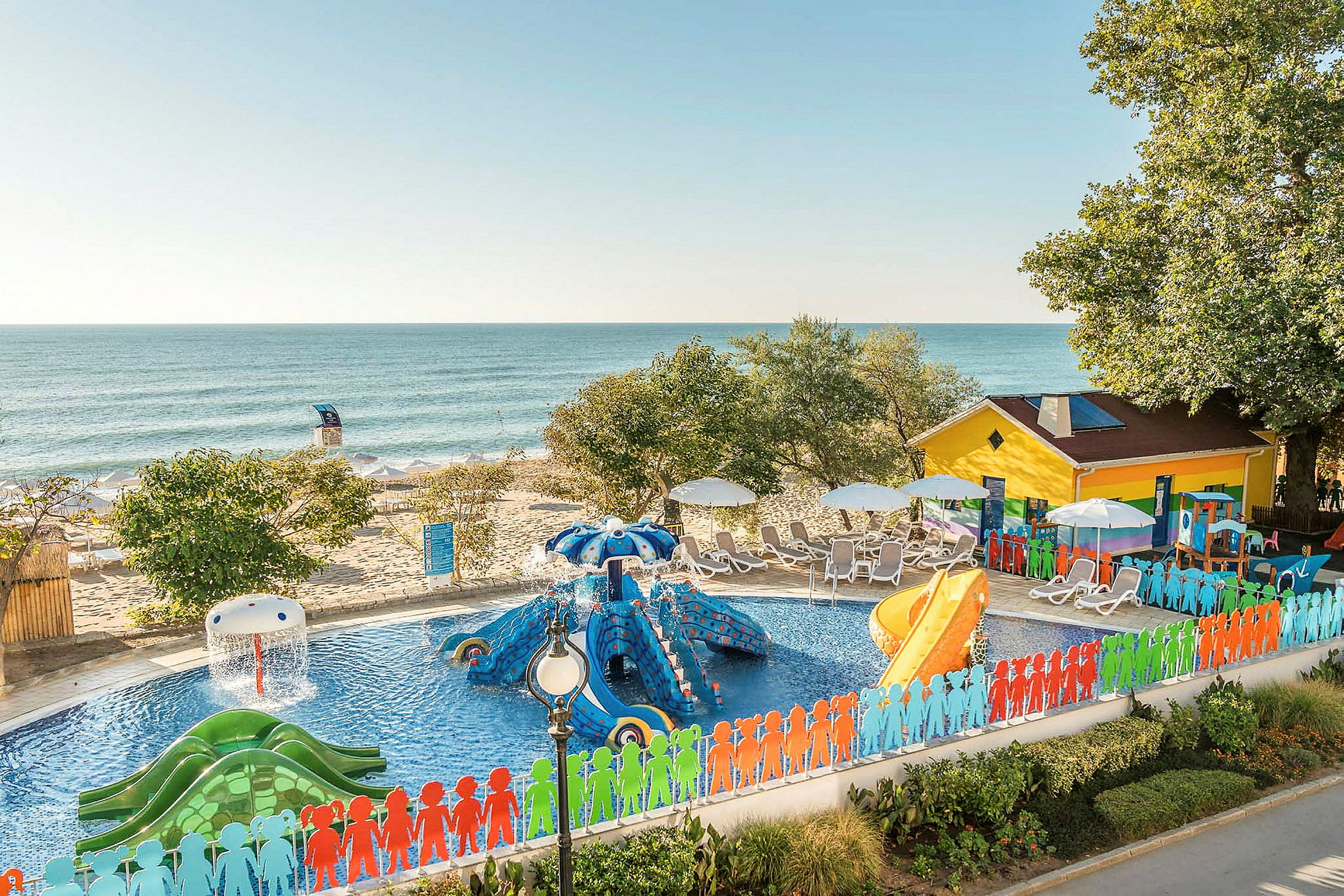 Färgglatt poolområde med vattenrutschkanor nära stranden med solstolar. (AI-genererad text)