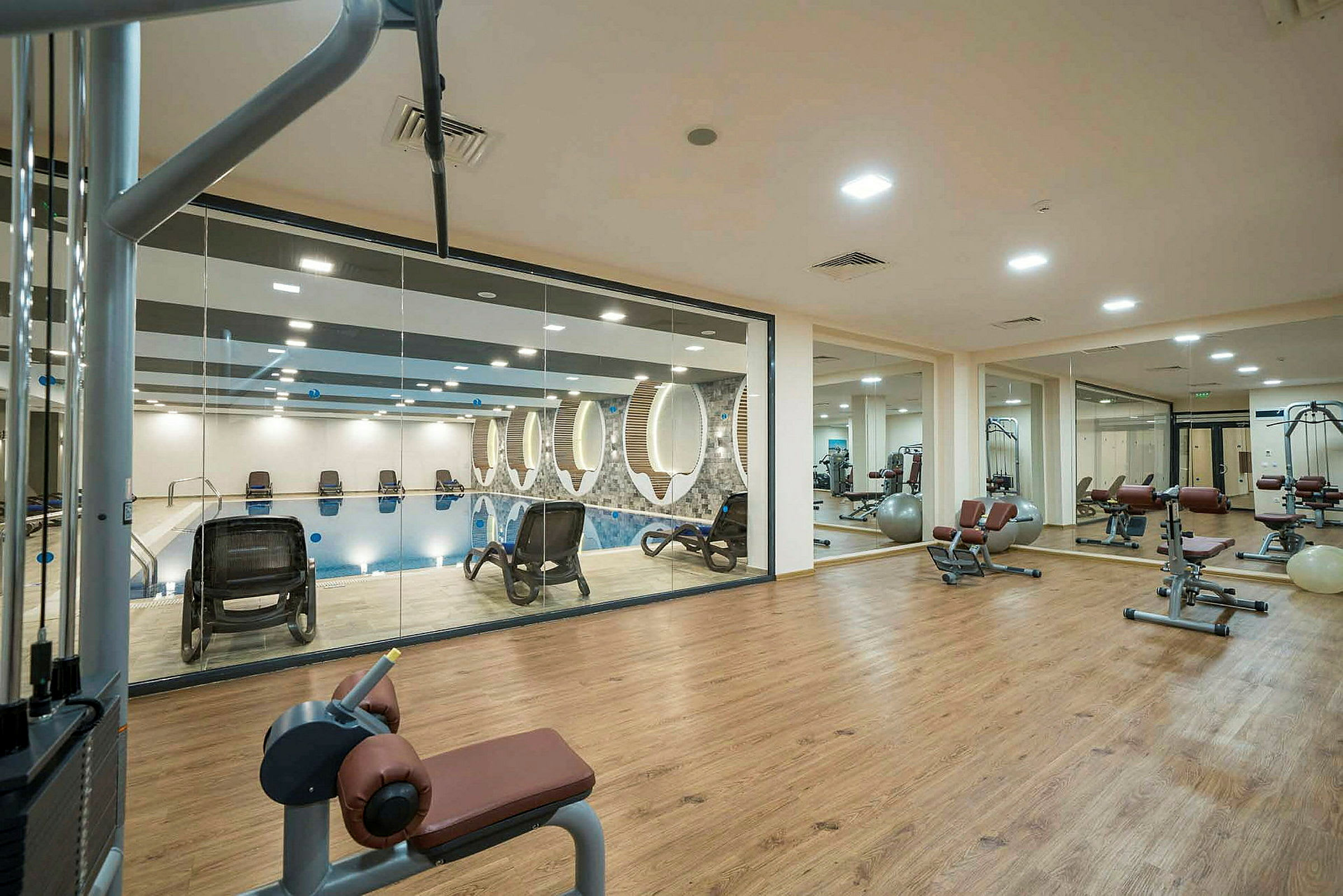Ett gym med träningsutrustning och glasvägg som vetter mot en pool. (AI-genererad text)