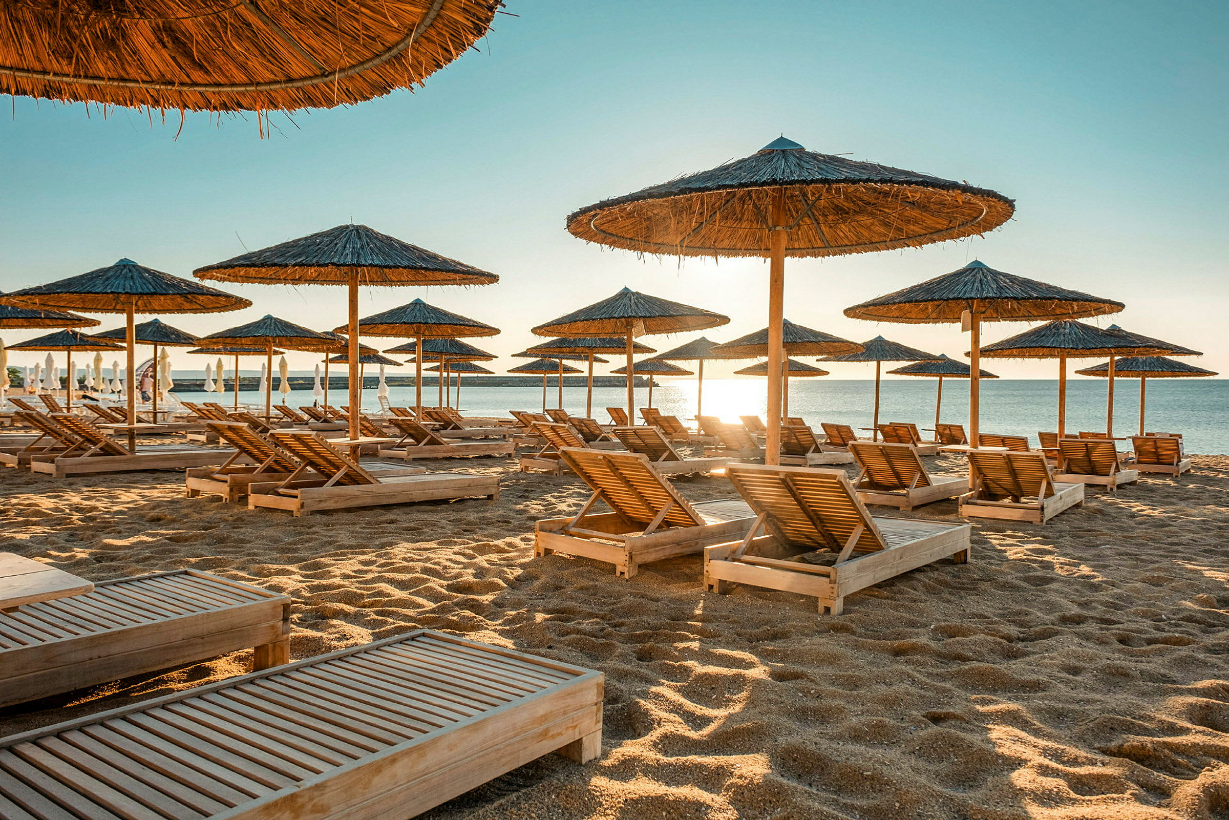 Strand med solsängar och parasoller av halm vid vattnet. (AI-genererad text)