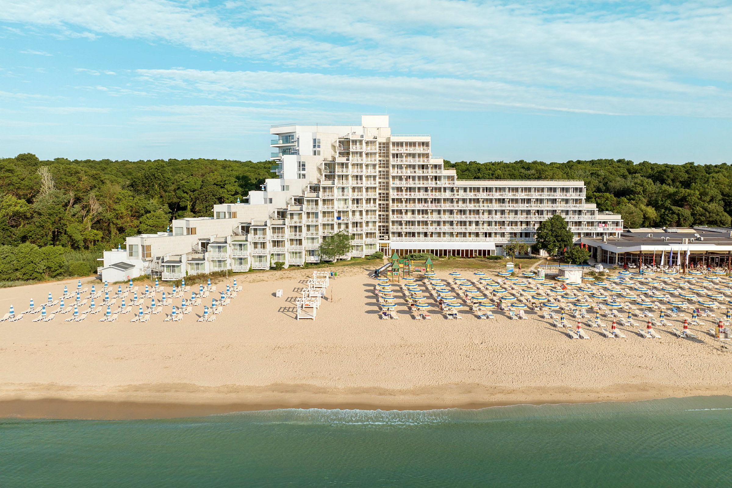 En strand med solstolar och parasoller framför ett hotell vid kusten. (AI-genererad text)
