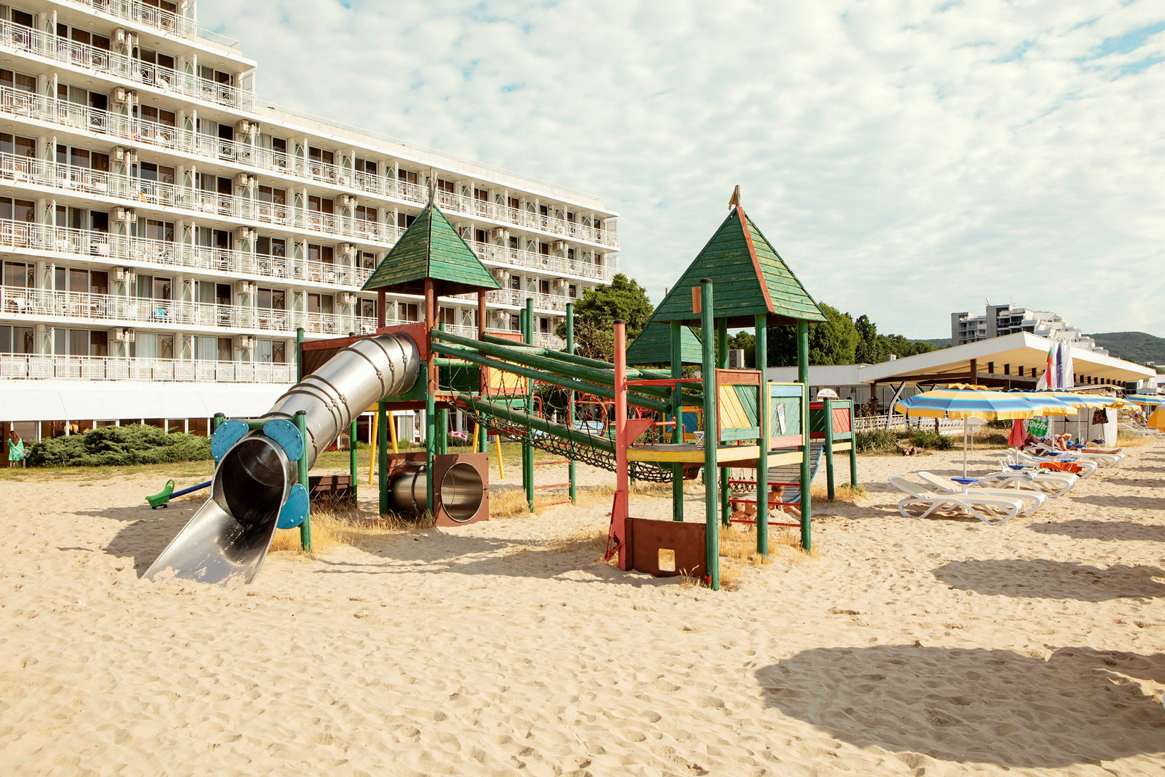 Lekplats med rutschkanor på sandstrand framför hotell. (AI-genererad text)