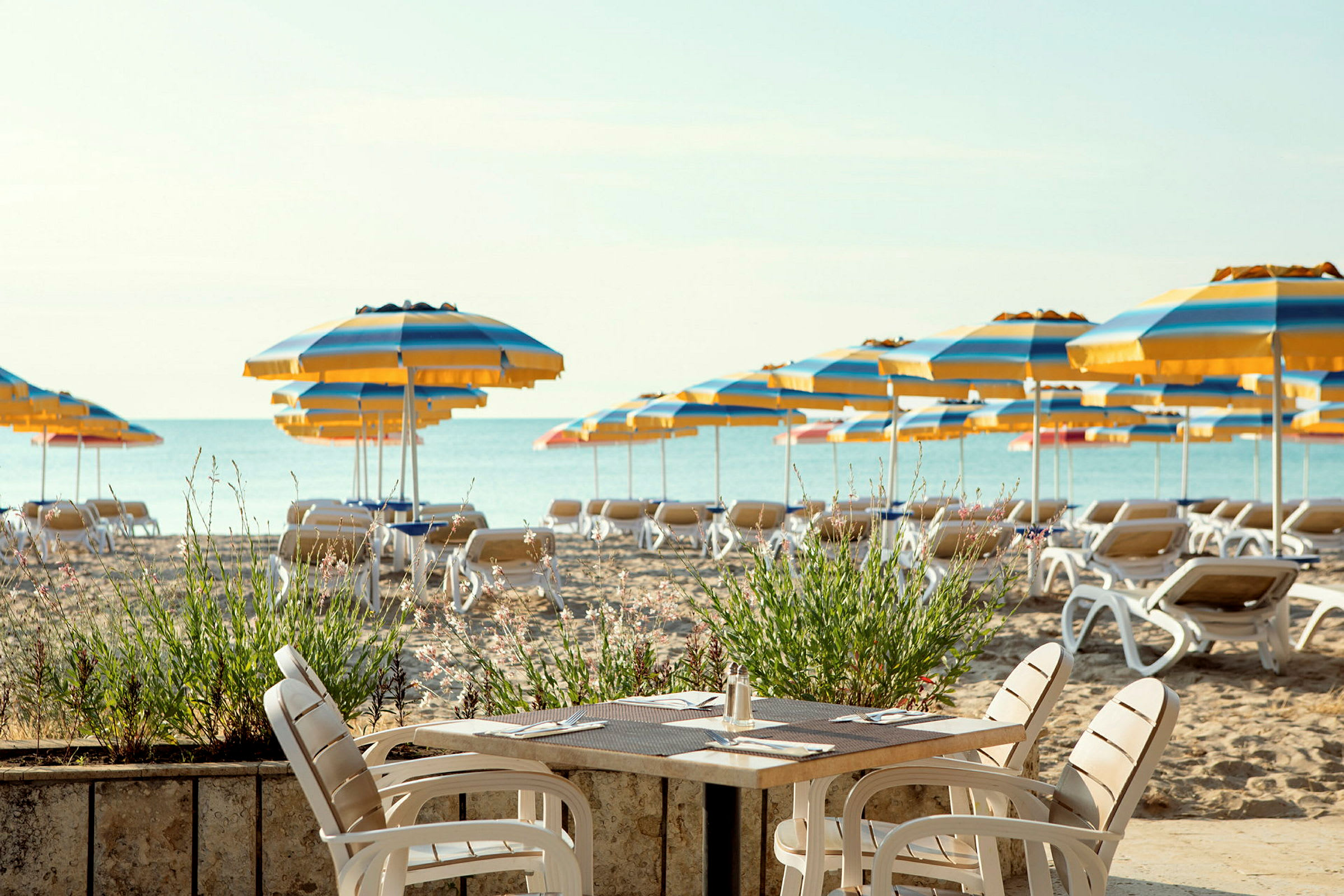 En strand med solstolar och flerfärgade parasoller, i förgrunden ett bord och stolar. (AI-genererad text)