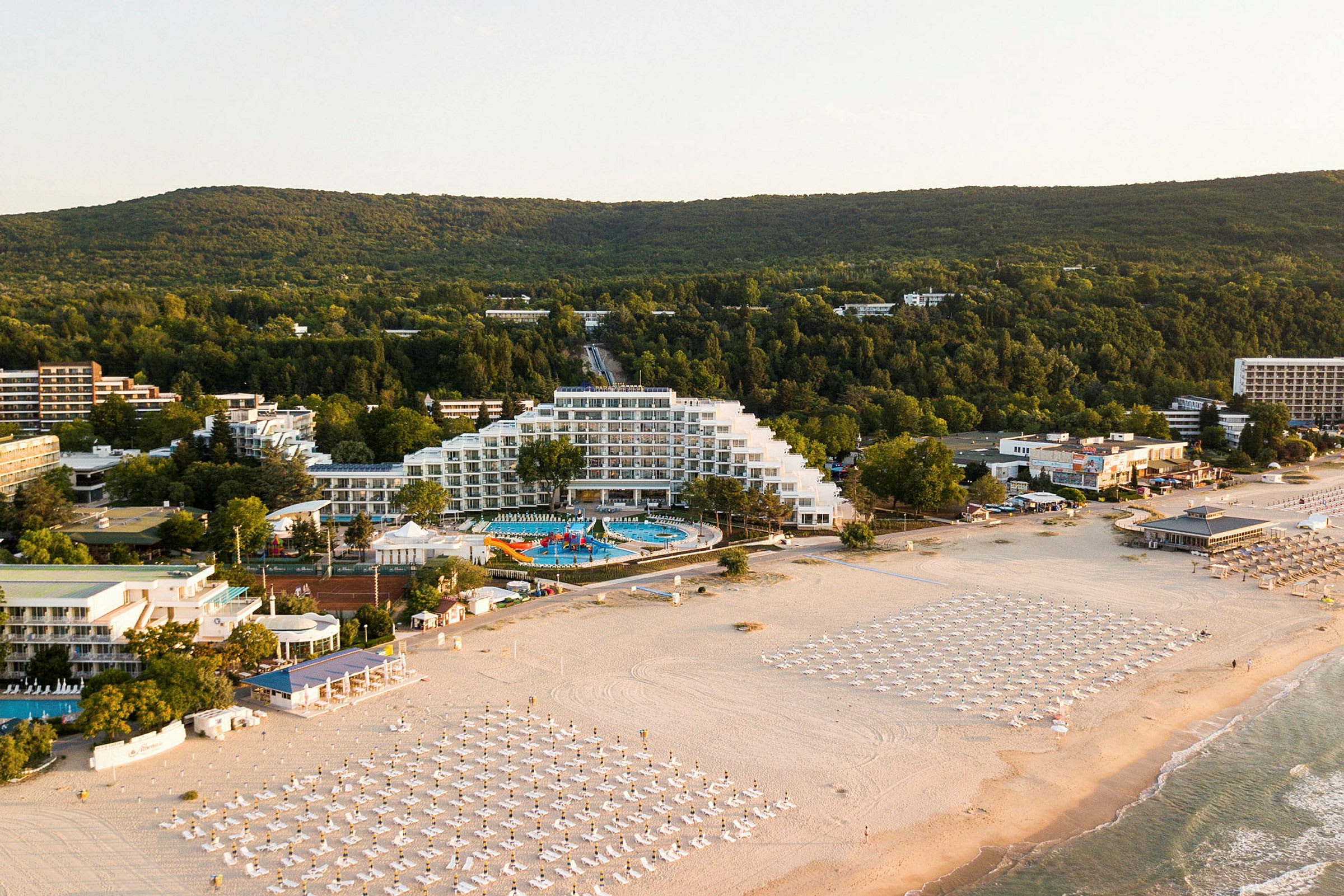 Bild av en kustnära semesterort med hotell, poolområde och strand med parasoller. (AI-genererad text)