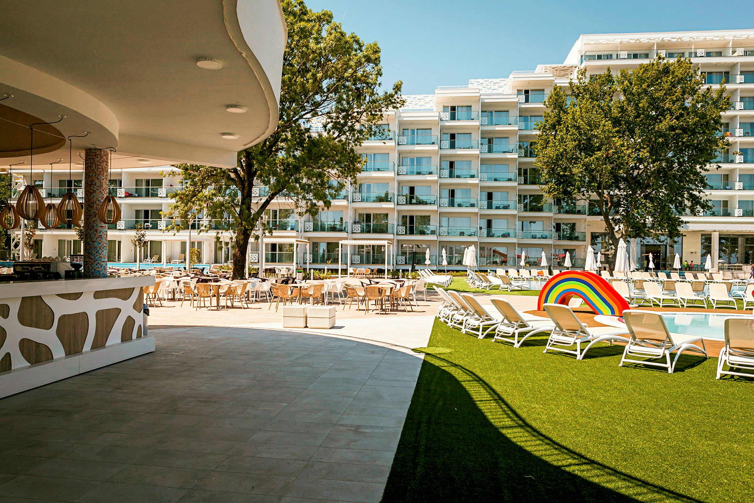 Hotellområde med pool, solstolar, gräsmatta och byggnader i bakgrunden. (AI-genererad text)