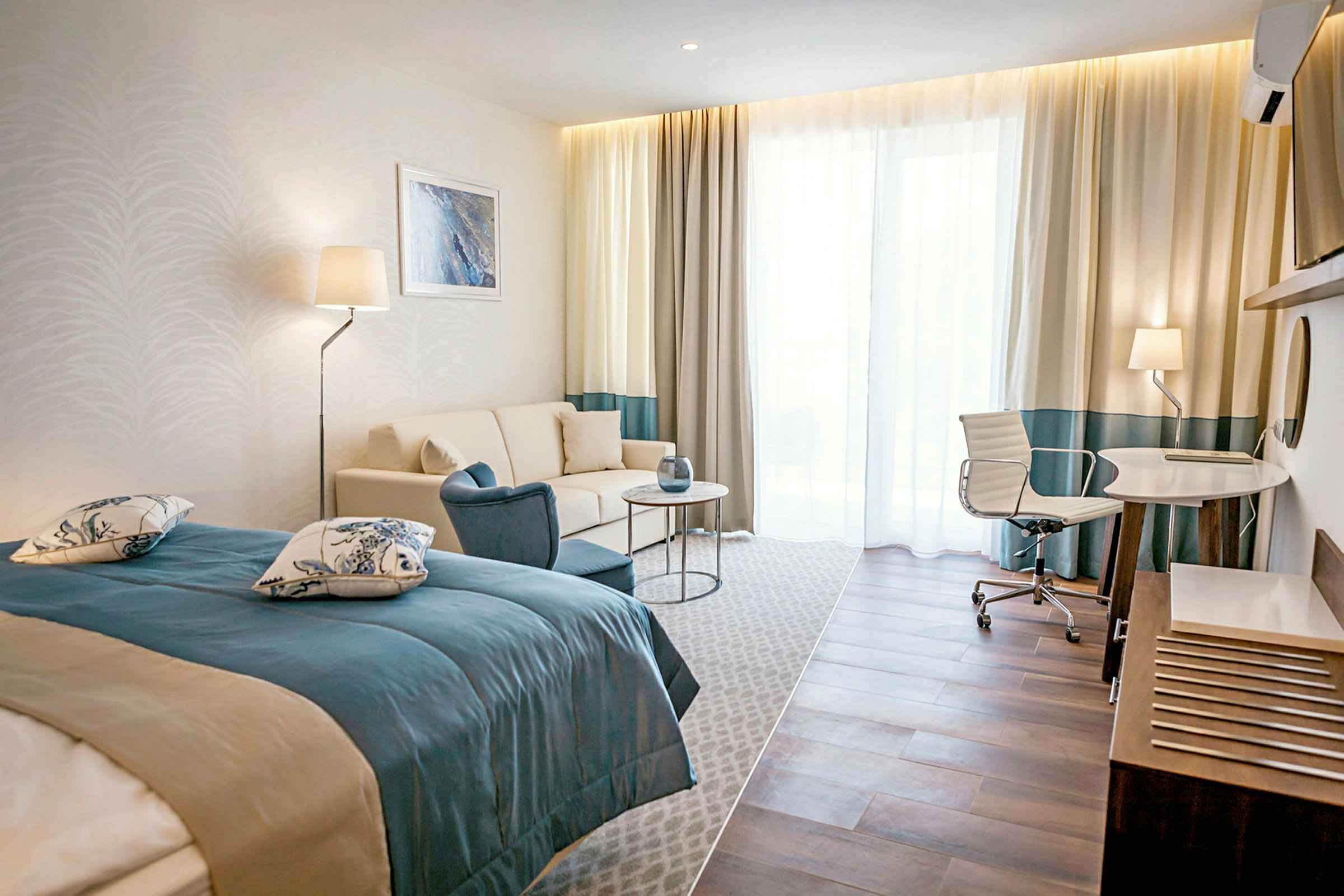 Ett hotellrum med en säng, soffa, bord och skrivbord med stol. (AI-genererad text)