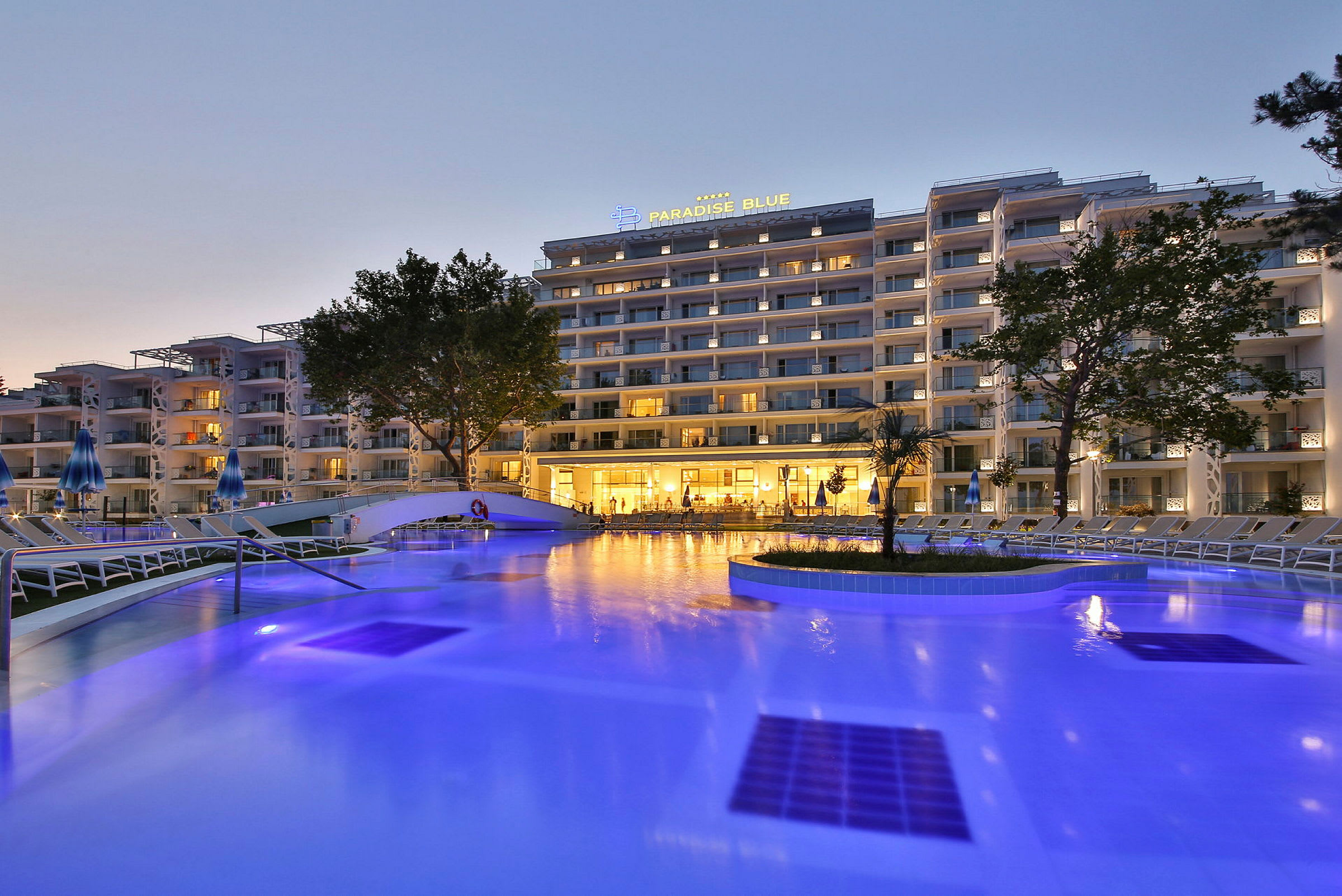 Ett upplyst hotell vid en pool på kvällen. (AI-genererad text)