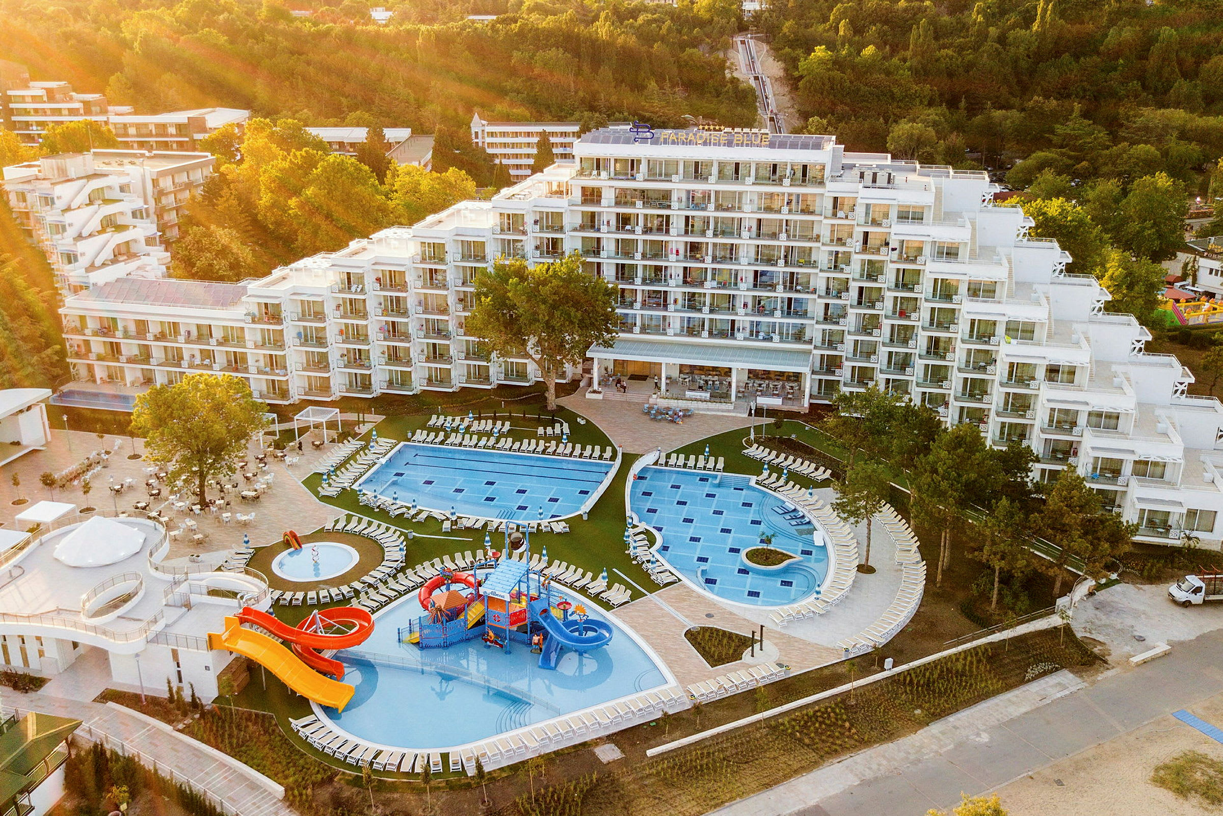 Hotell med poolområde, vattenrutschbanor och grönska runtomkring. (AI-genererad text)