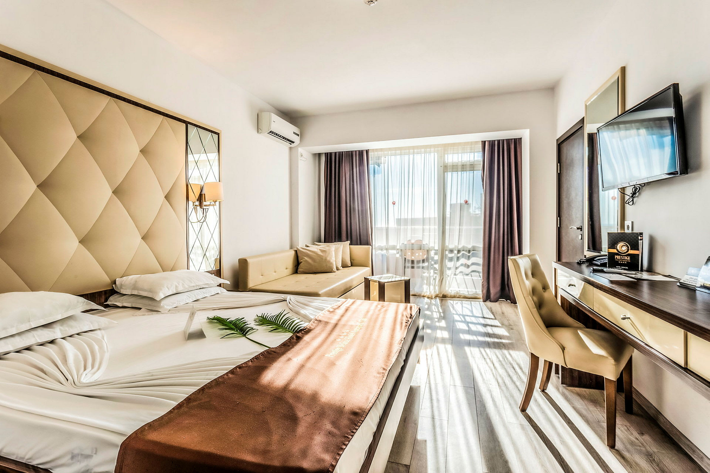 Ett hotellrum med en bred säng, ett skrivbord, en stol, en soffa och en TV. Rummet har stora fönster med utsikt. (AI-genererad text)
