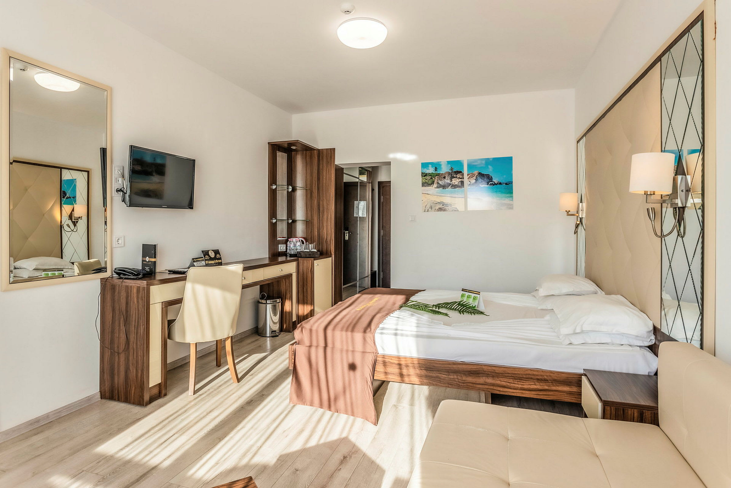 Ett hotellrum med en dubbelsäng, skrivbord, väggmonterad TV och spegel, samt ett stort fönster som släpper in naturligt ljus. (AI-genererad text)