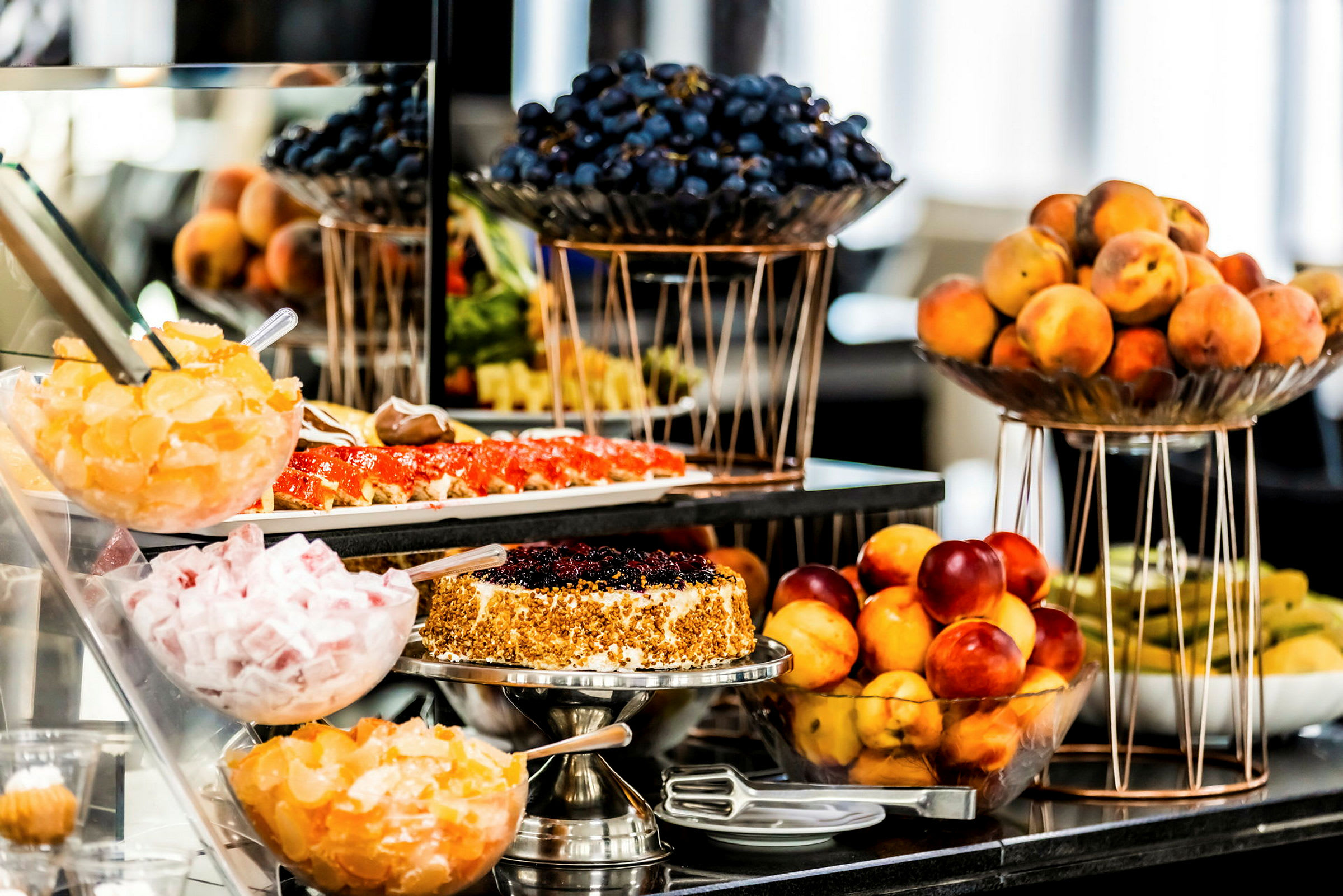 Ett bord fyllt med färska frukter och desserter, inklusive glas med små mandariner, en tårta med bär och skålar med vindruvor och persikor. (AI-genererad text)