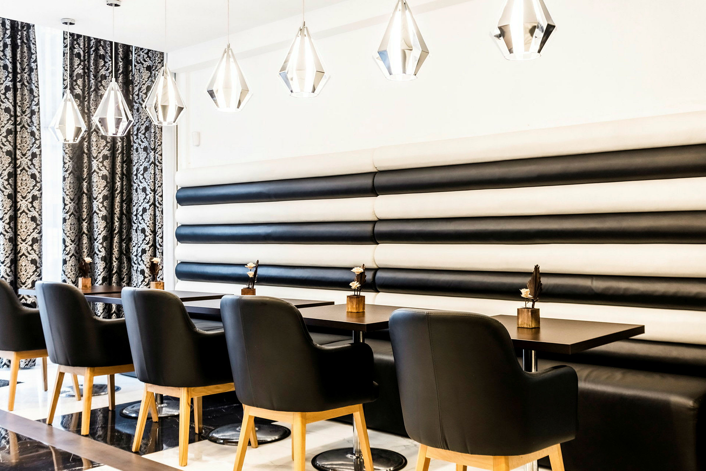 En modern restaurang med svart och vit inredning. Svarta stolar med träben står vid bord med dekorativa föremål. (AI-genererad text)