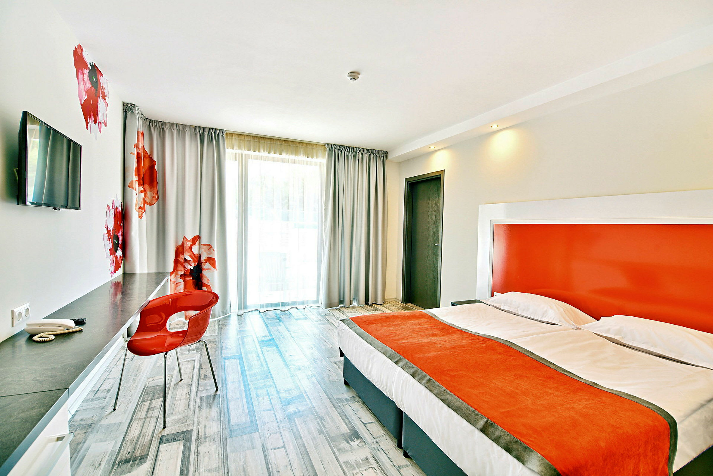 Modernt hotellrum med orange detaljer, bekväm säng och skrivbord område. (AI-genererad text)