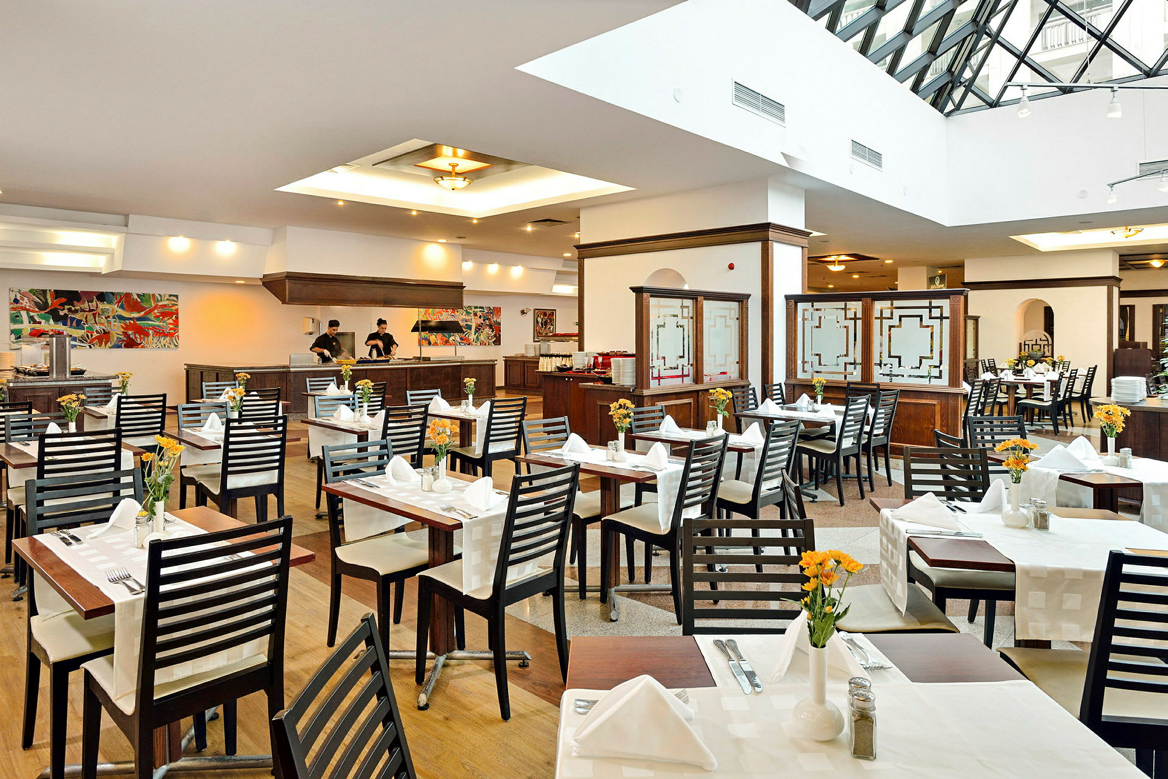 Interiör av en restaurang med bord uppställda och dukade samt personal vid serveringsdisken. (AI-genererad text)