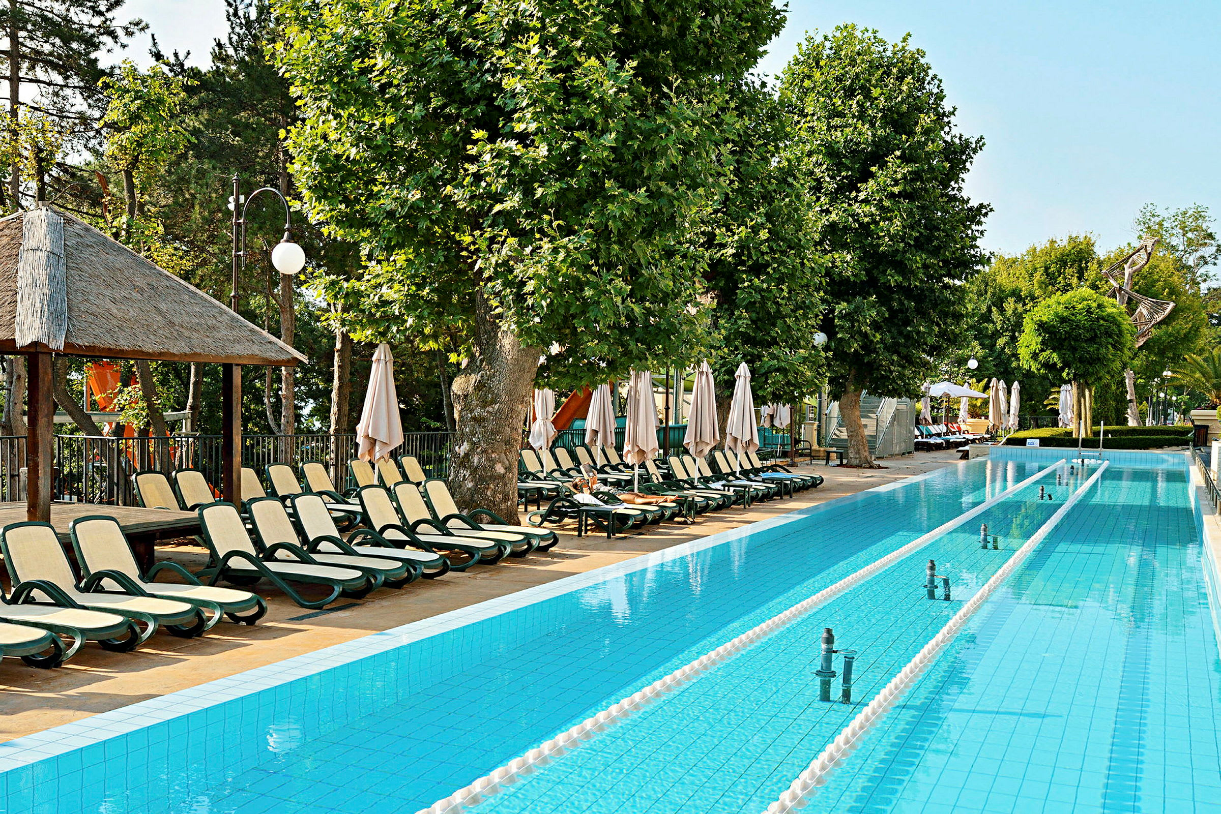 Poolområde med solstolar och parasoller vid sidan av en långt rektangulär pool. (AI-genererad text)