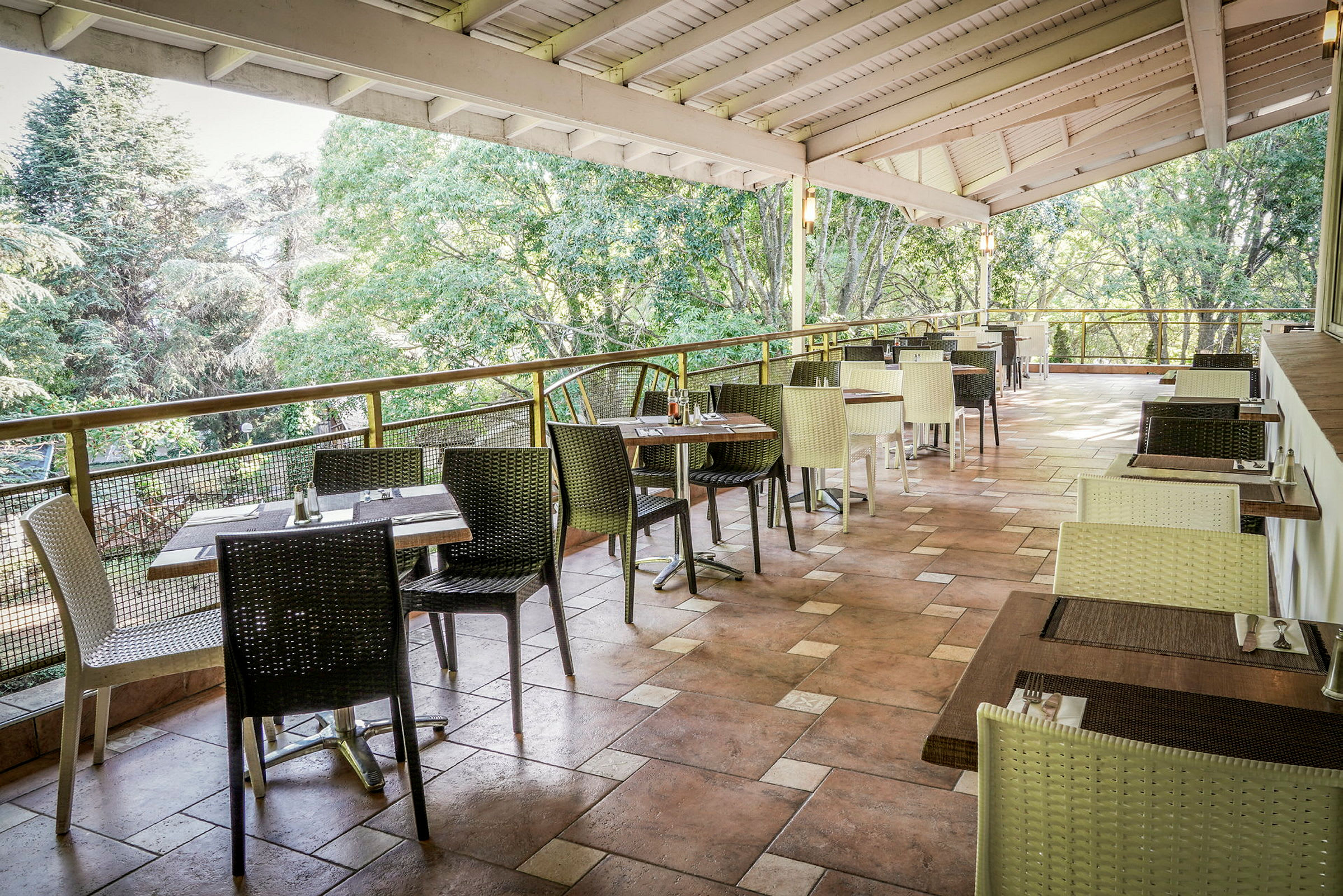 En öppen restaurangterrass med bord och stolar, omgiven av grönskande träd. (AI-genererad text)