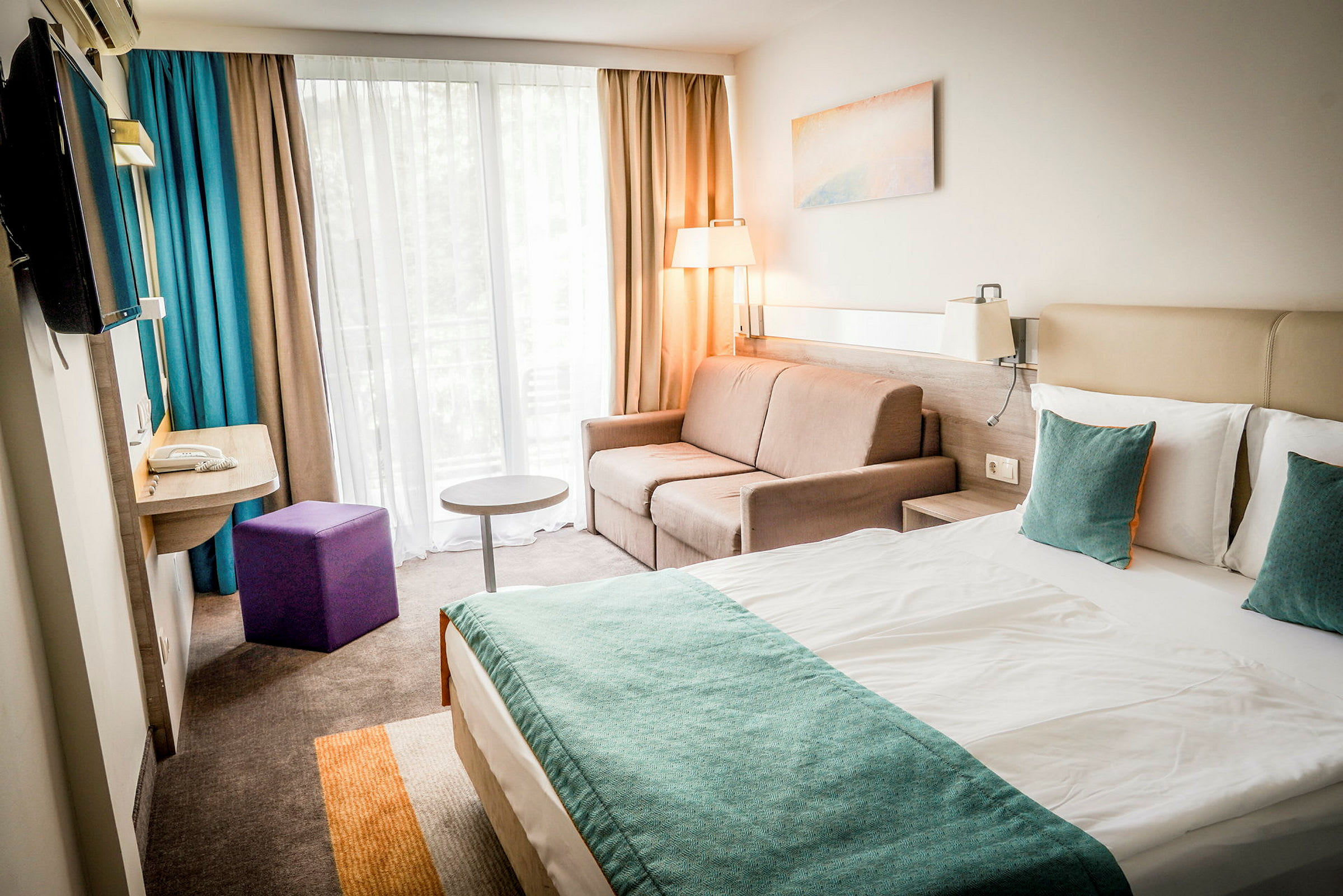En modern hotellrum med en dubbelsäng, soffa, och fönster med gardiner. (AI-genererad text)