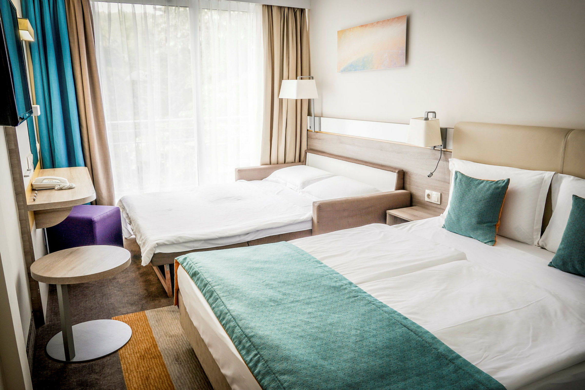 Två sängar i ett hotellrum, med en stor fönstervägg och gardiner. (AI-genererad text)