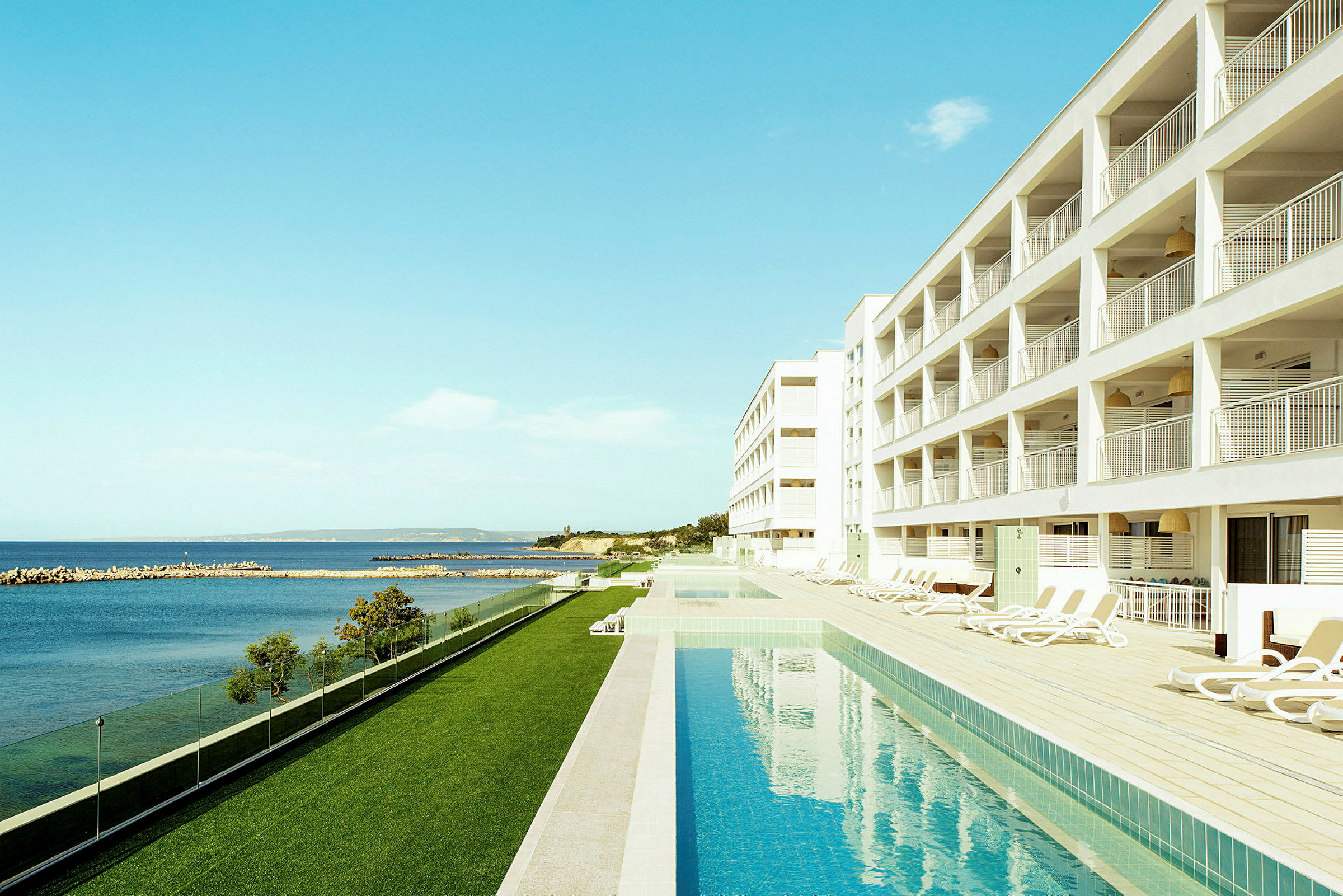 Hotell med pool vid havet och solstolar bredvid. (AI-genererad text)