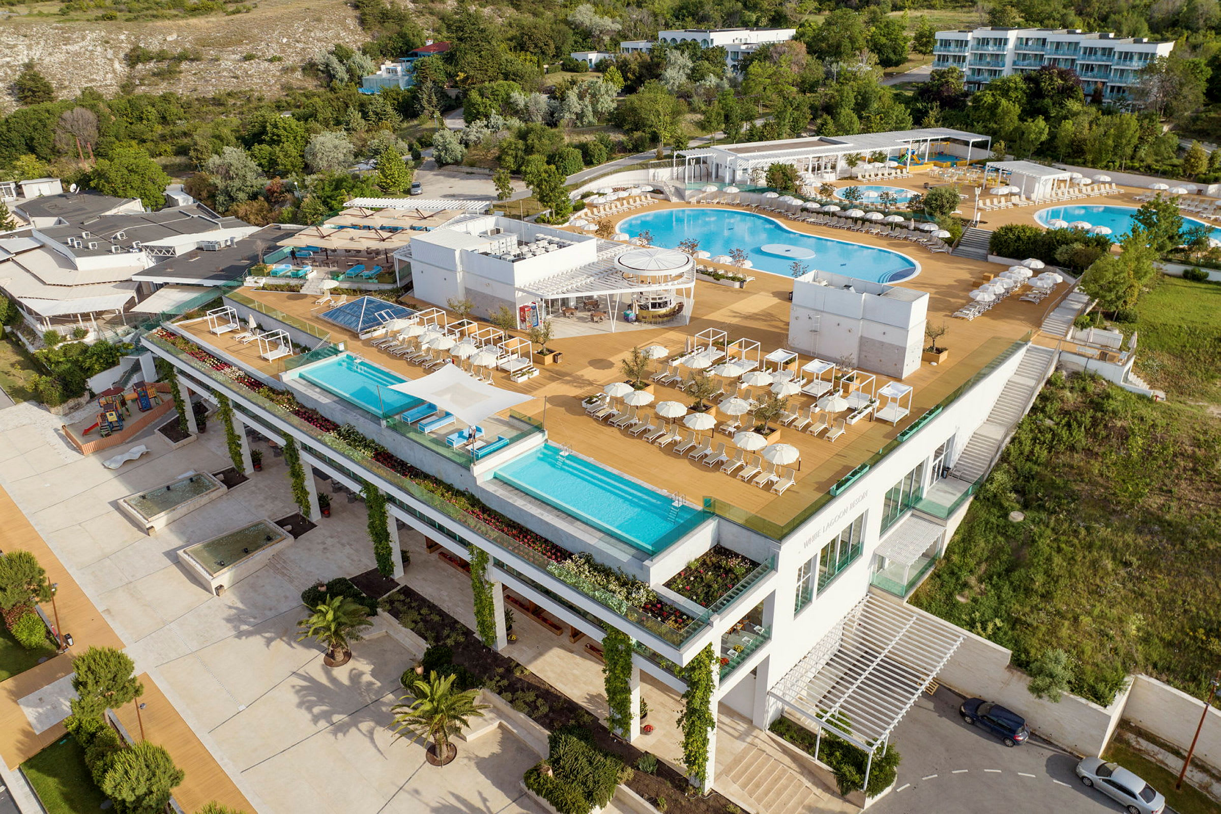 En modern hotellresort med flera utomhuspooler, solstolar och parasoller, omgiven av grönska. (AI-genererad text)