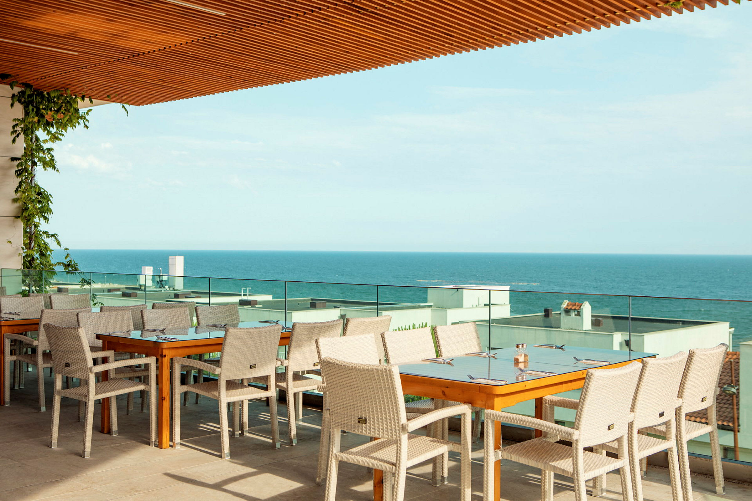 Restaurangbord och stolar på en terrass med utsikt över havet. (AI-genererad text)