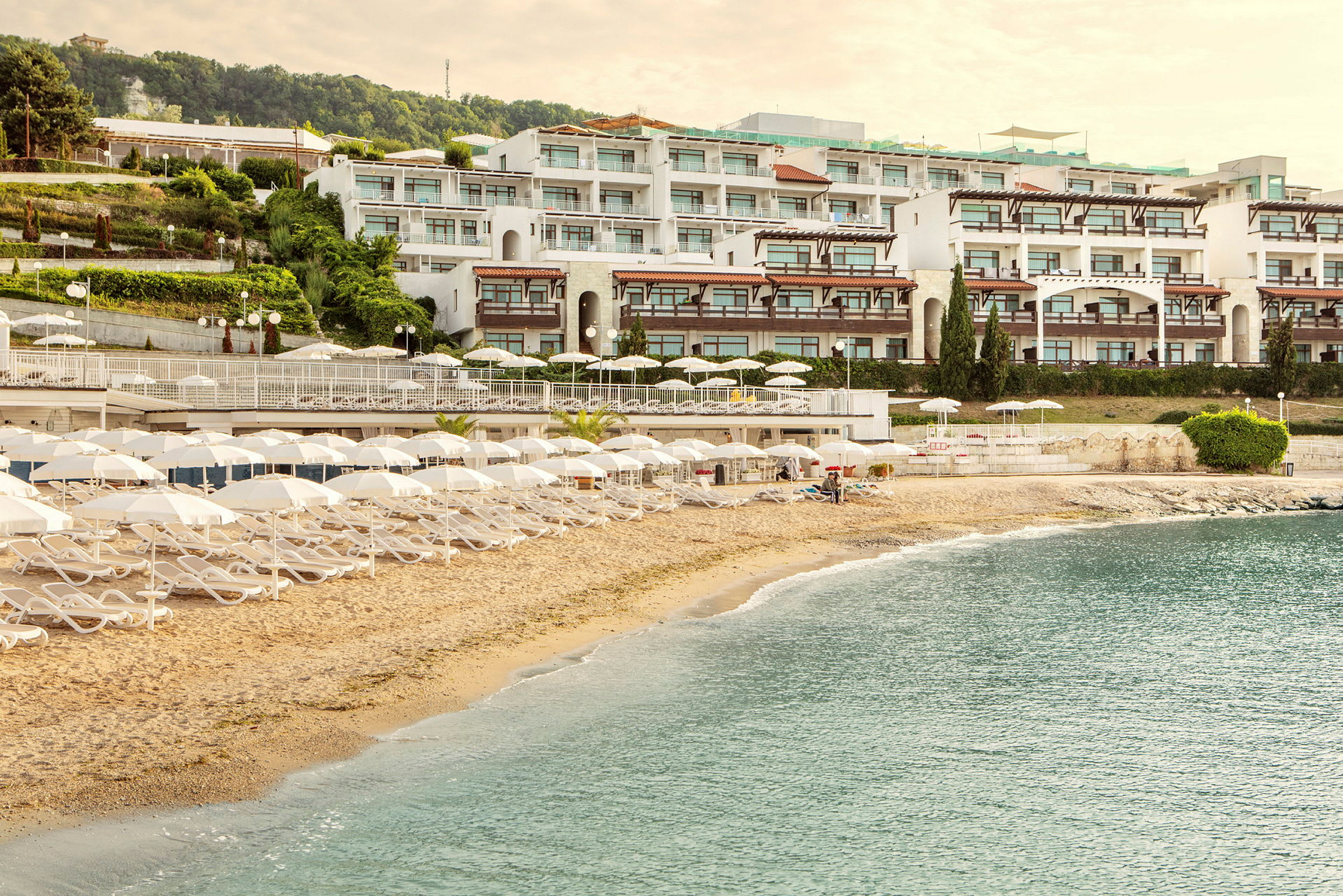 En sandstrand med solstolar och parasoller framför ett hotellkomplex. (AI-genererad text)
