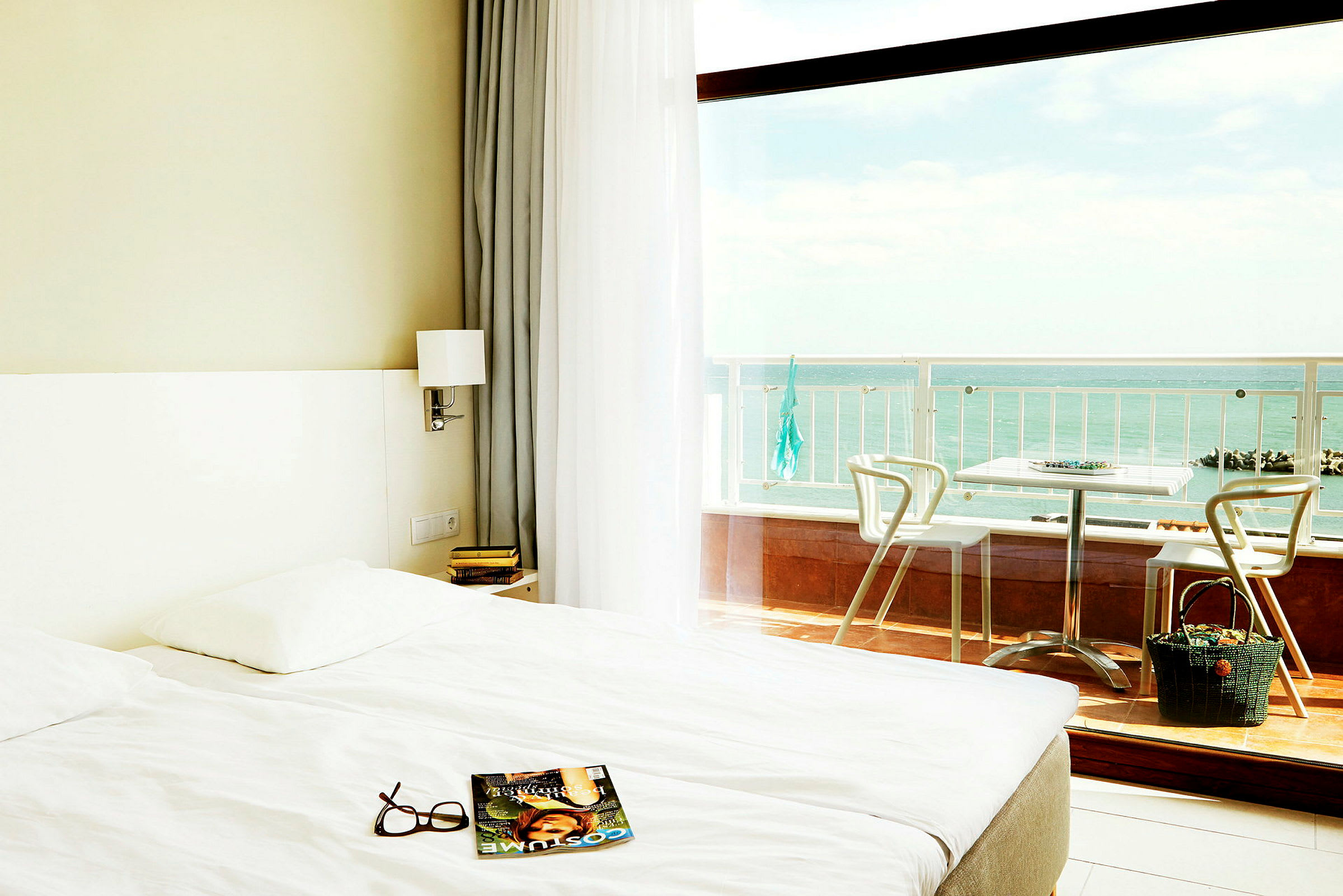 Ett hotellrum med en stor säng och glasdörrar som vetter mot en balkong med utsikt över havet. (AI-genererad text)
