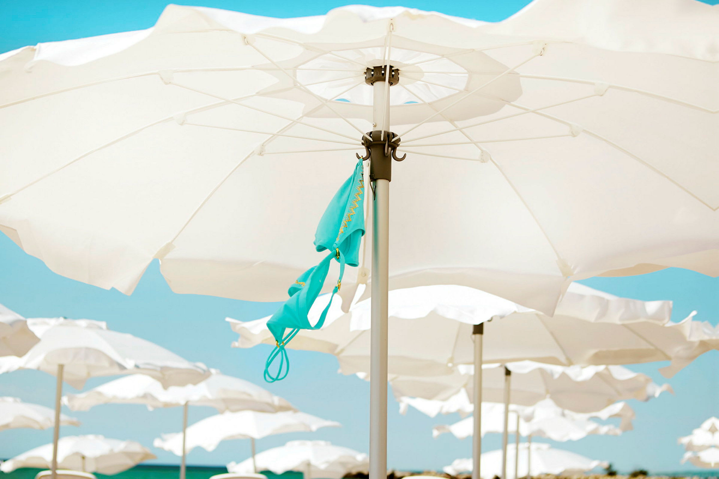 Paraplyer på en strand med en turkos bikiniöverdel hängande från ett av paraplyerna. (AI-genererad text)
