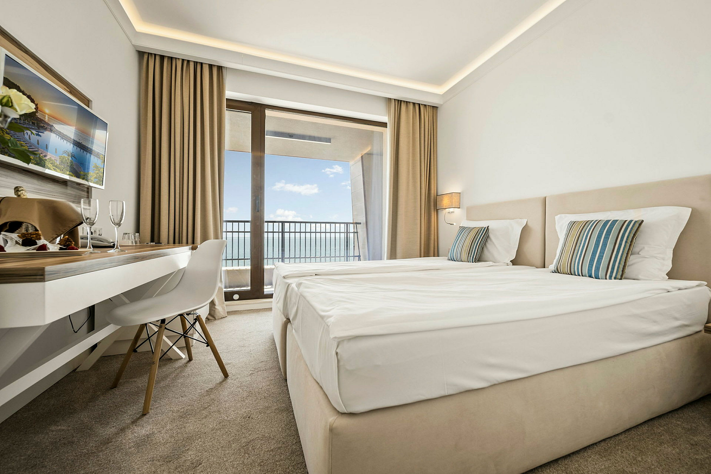 Hotellrum med två sängar, skrivbord och balkong med utsikt över havet. (AI-genererad text)