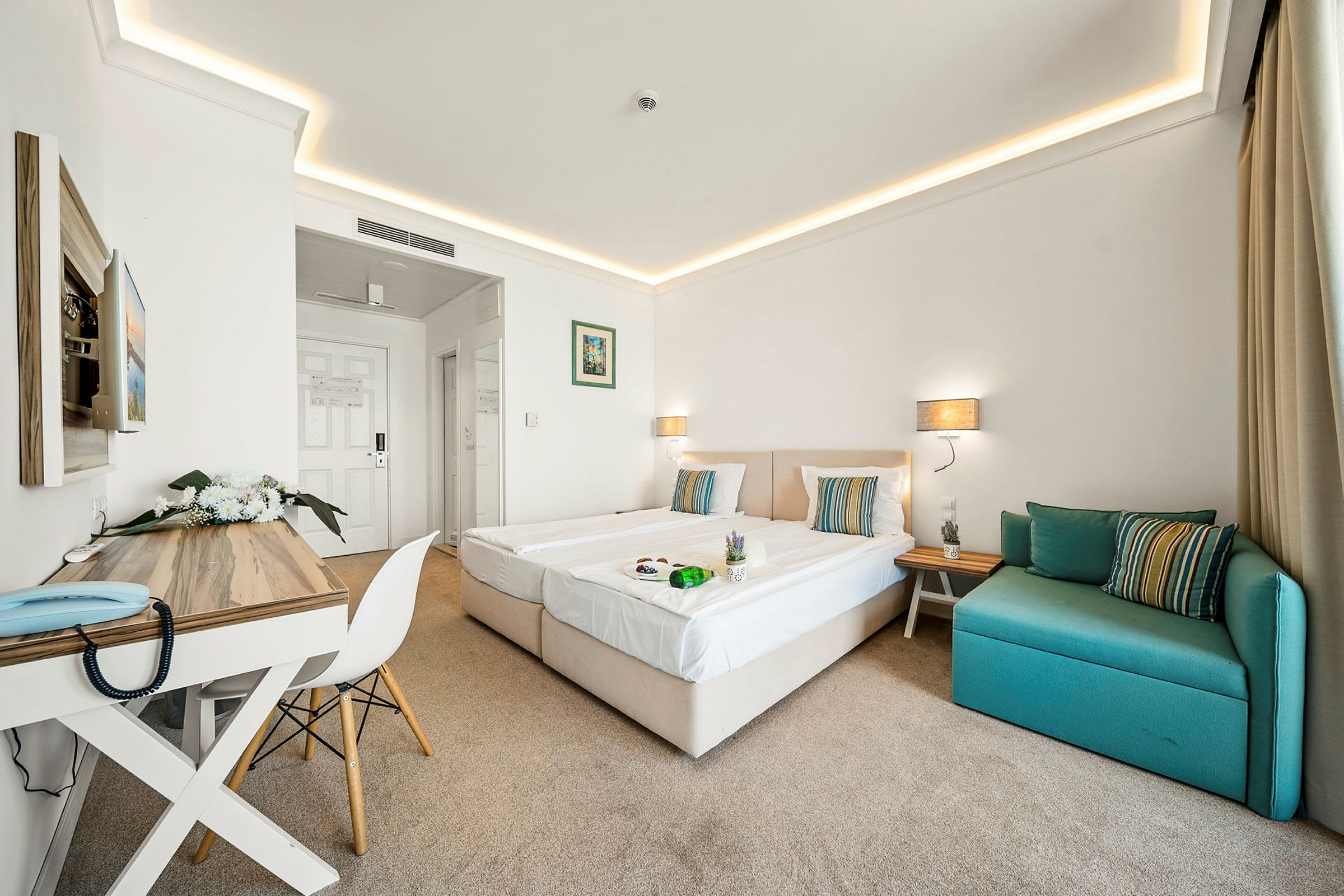 Ett hotellrum med två enkelsängar, ett skrivbord och en grön soffa. (AI-genererad text)