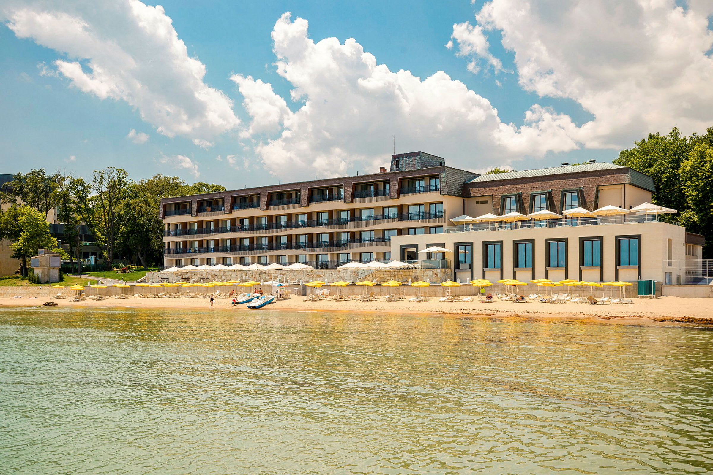 Flerfaldigt våningshotell vid stranden med gula parasoller och klarblå himmel. (AI-genererad text)
