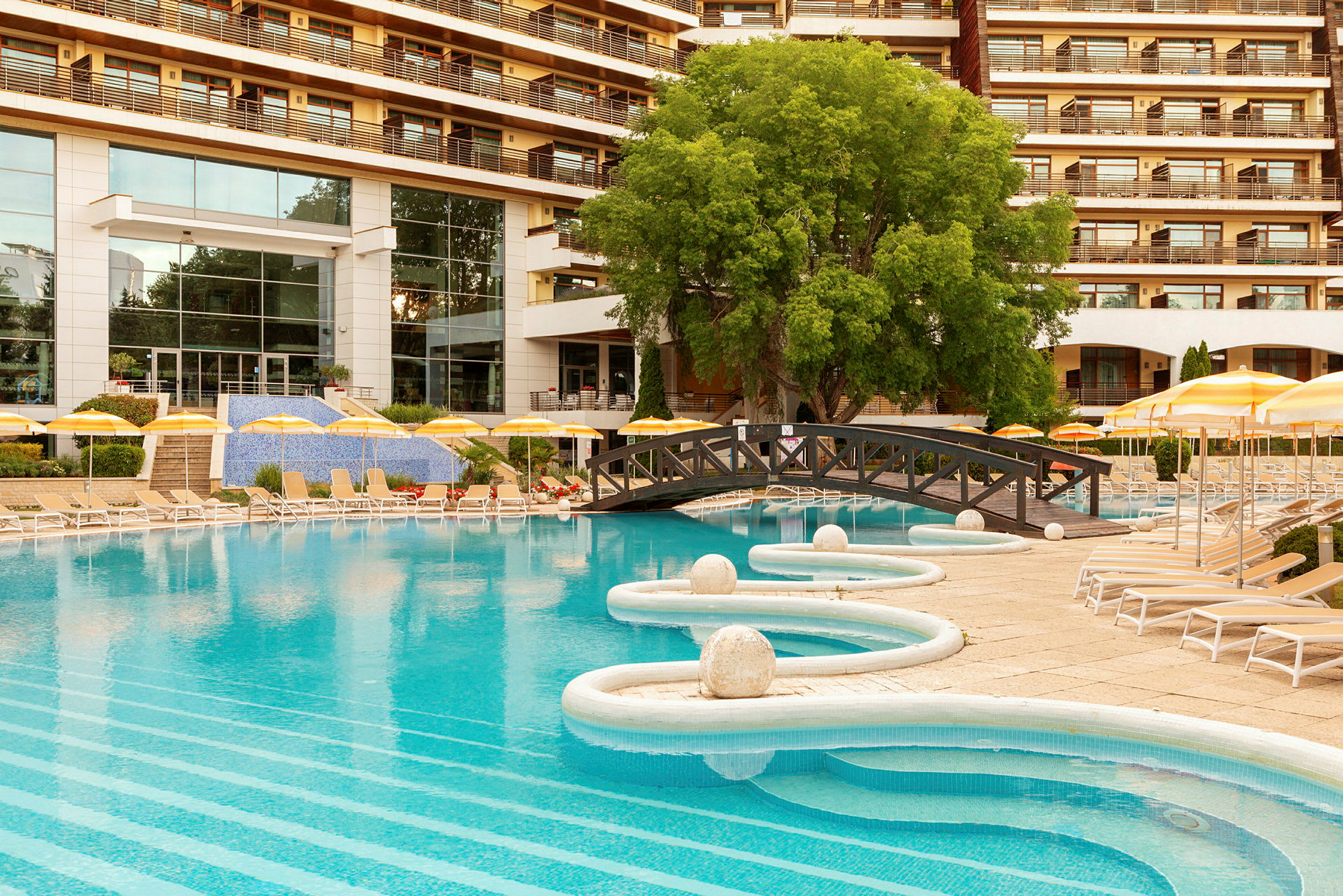 En utomhuspool med solstolar och parasoller framför ett hotell. (AI-genererad text)