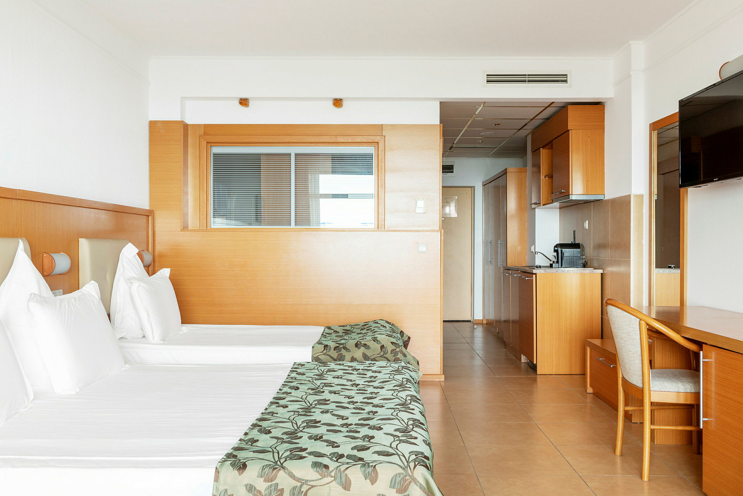 Hotellrum med två enkelsängar, köksdel och skrivbord. (AI-genererad text)