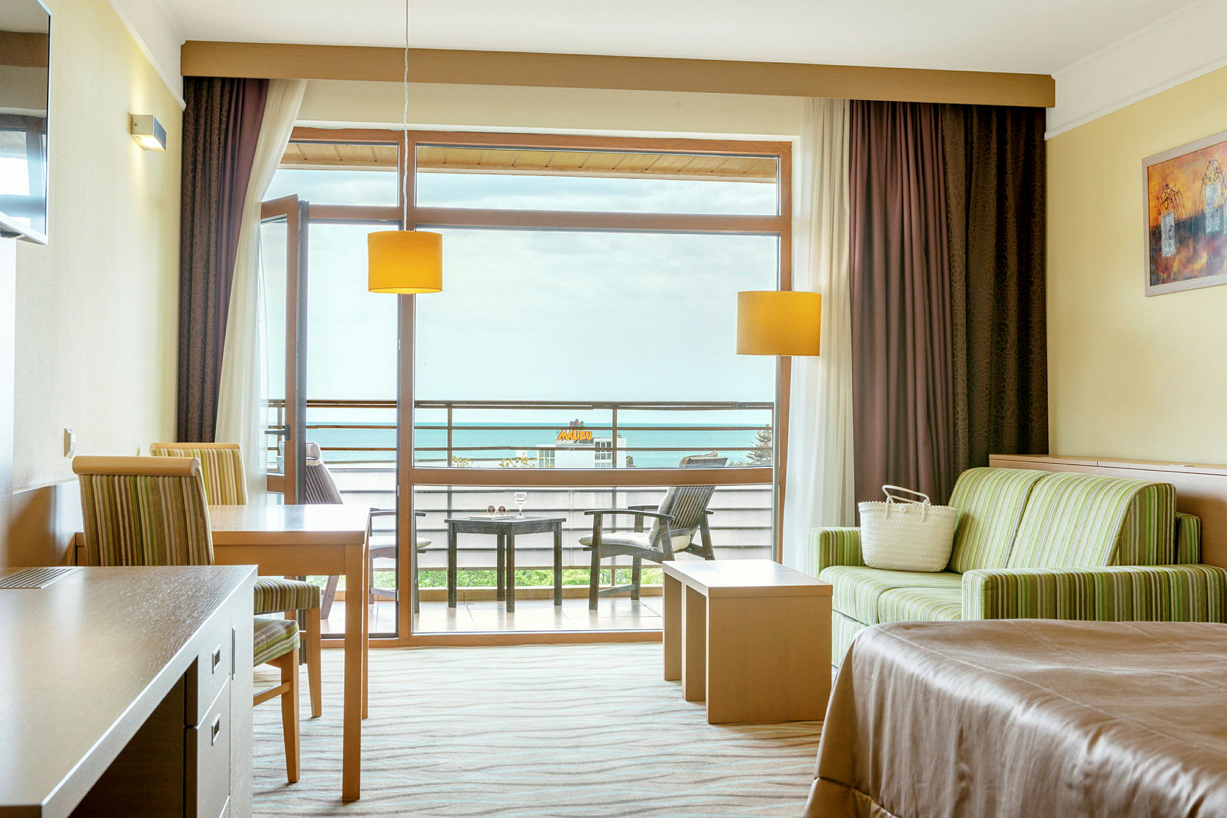 Ett hotellrum med sittområde, bord, säng och balkong med utsikt. (AI-genererad text)
