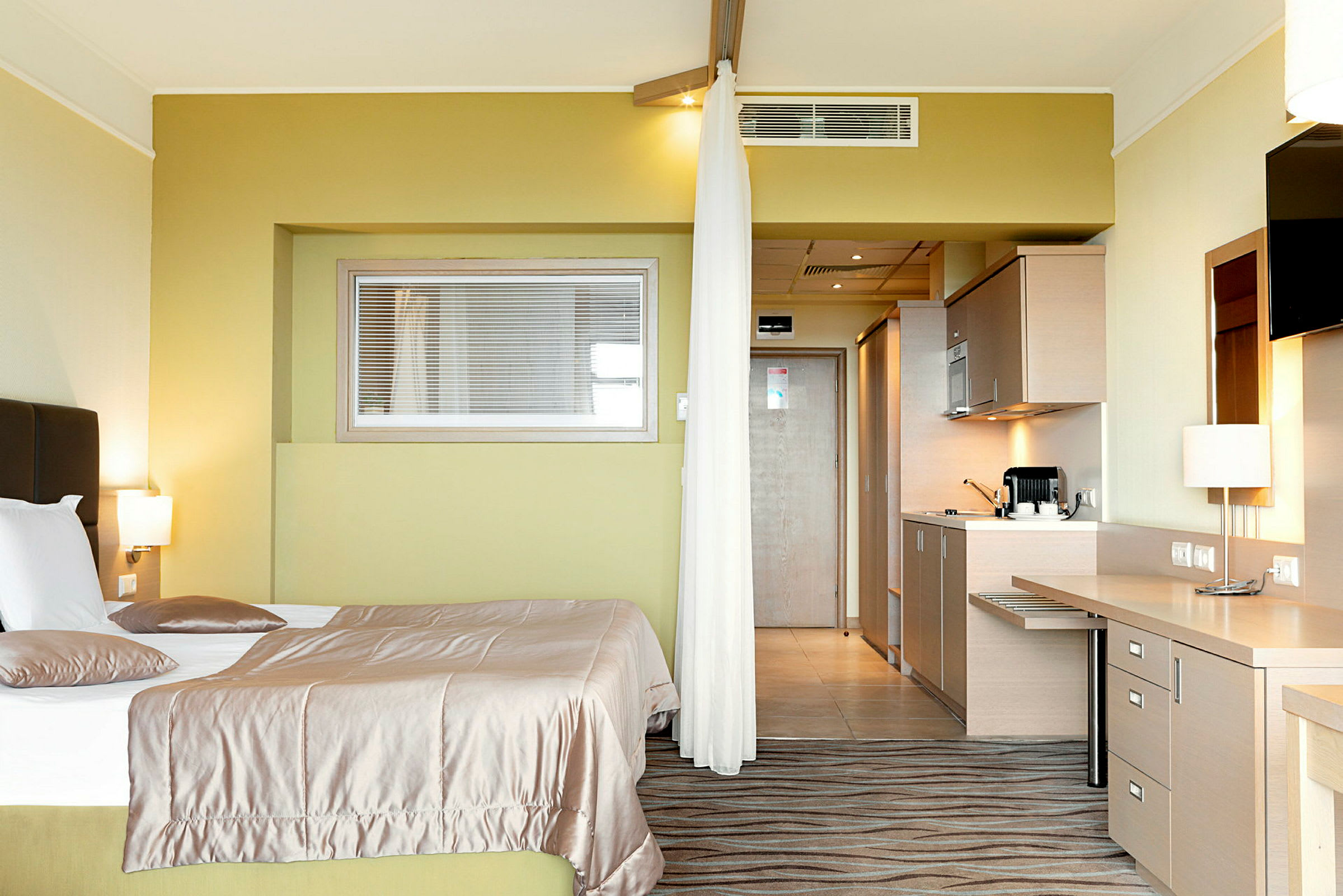 Ett hotellrum med en säng, skrivbord och köksdel. (AI-genererad text)