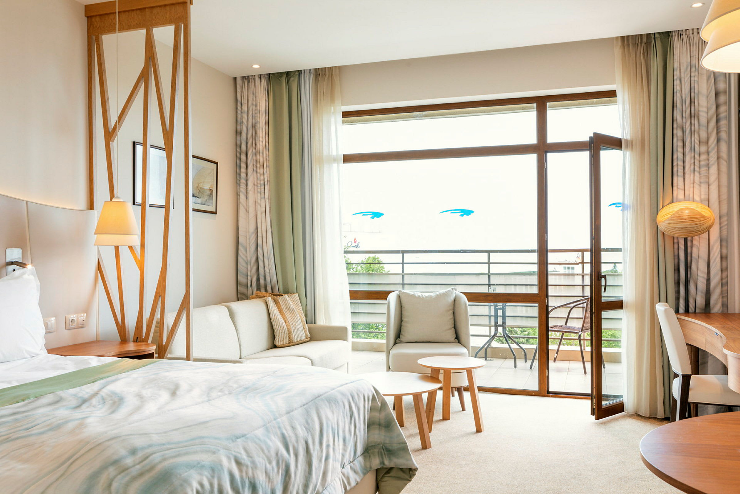 Ett hotellrum med säng, sittgrupp, bord och öppen balkongdörr. (AI-genererad text)