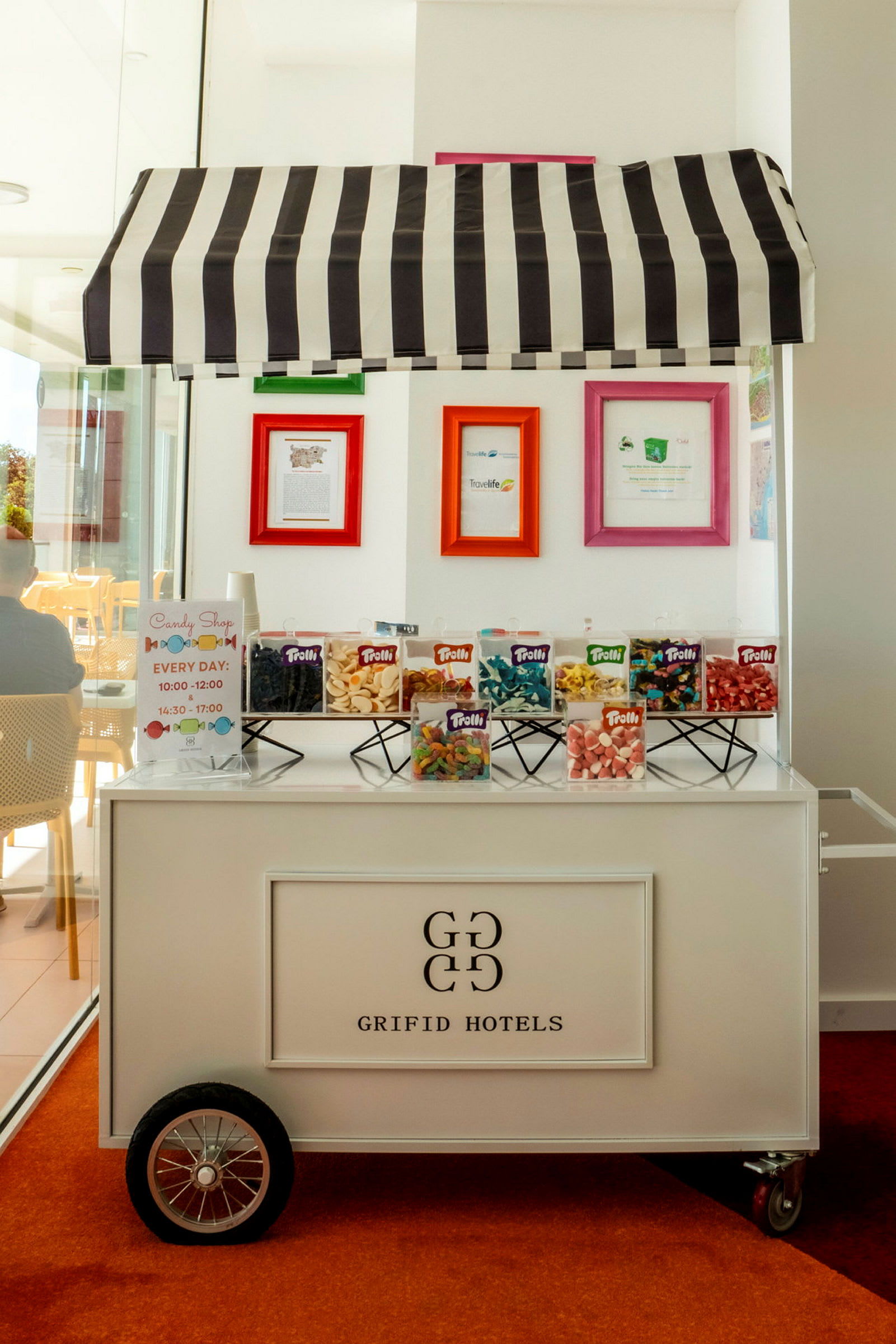 En godiskiosk med märkningen 'Grifid Hotels' och en randig markis, där olika sorter av godis är utställda. (AI-genererad text)