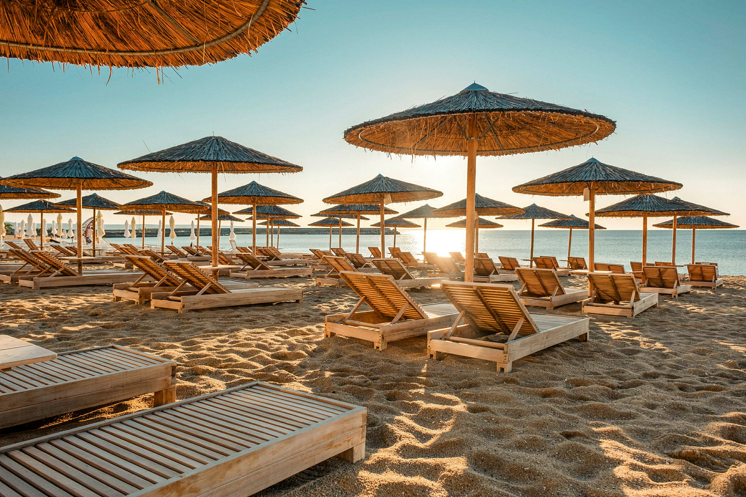 Strand med solsängar och parasoller i trä. (AI-genererad text)