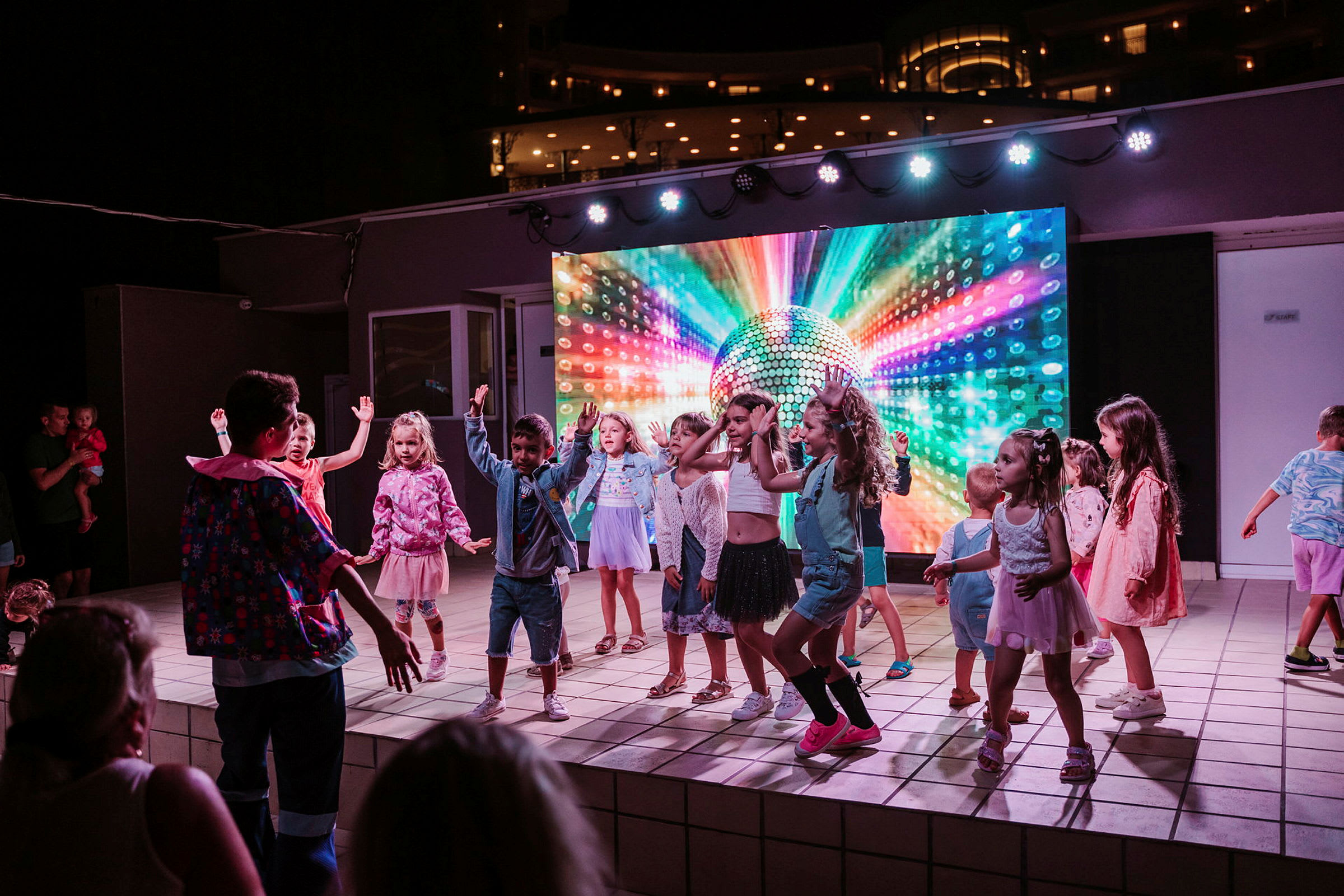Barn dansar på en scen med färgglad bakgrundsbild av en discokula. (AI-genererad text)
