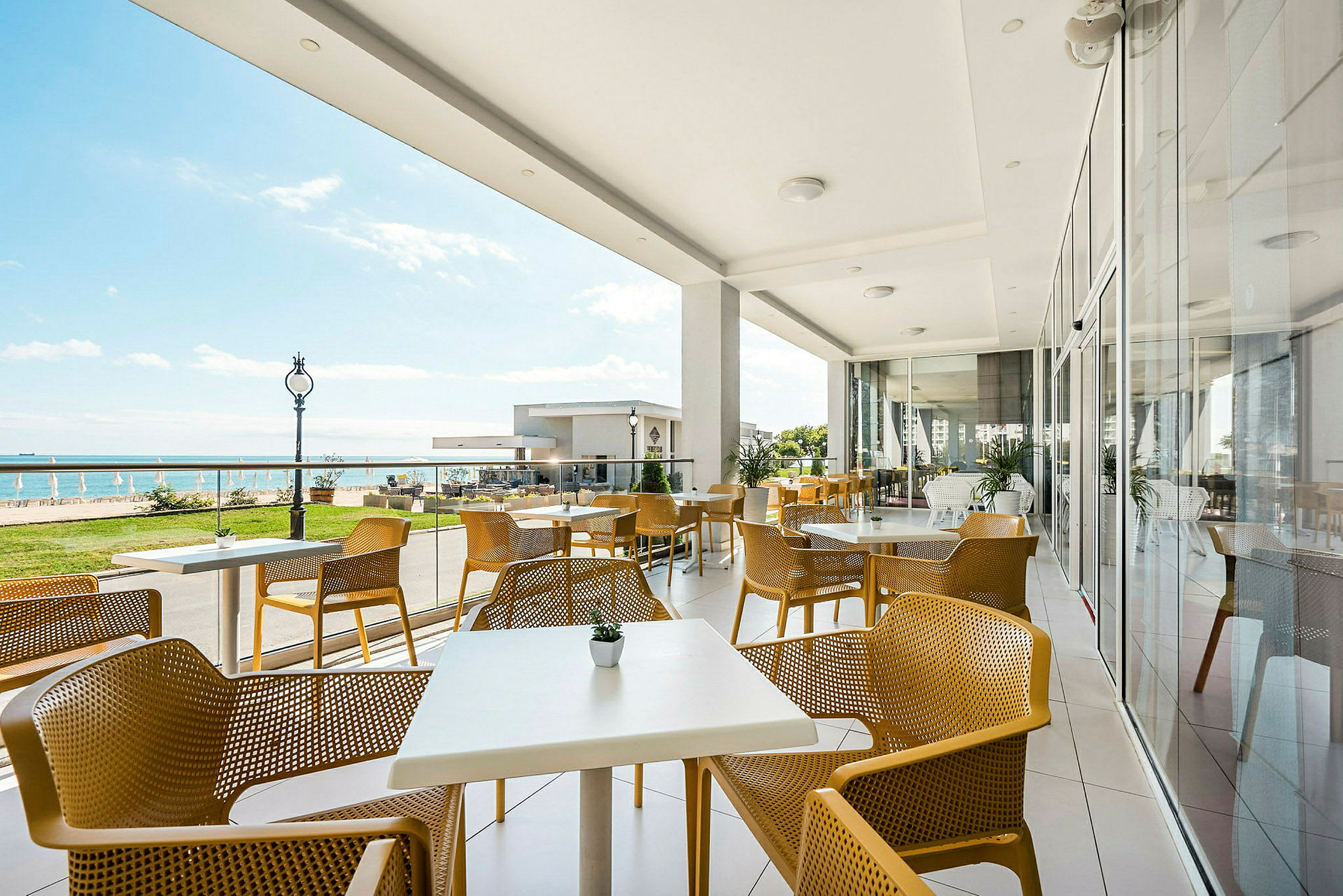 En uteservering med gula stolar och vita bord vid havet. (AI-genererad text)