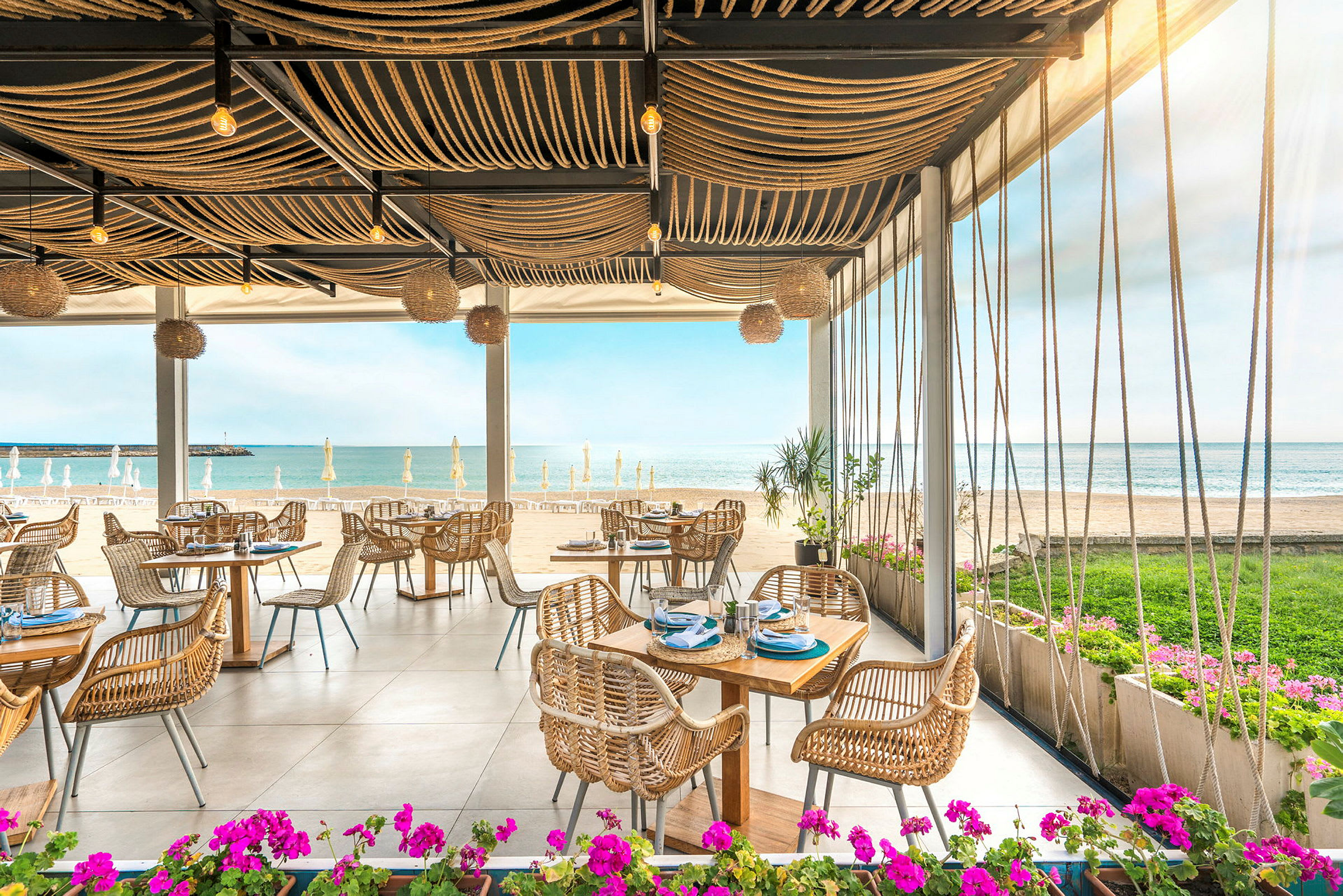 Restaurang vid stranden med utsikt över havet och bord med rottingstolar. (AI-genererad text)