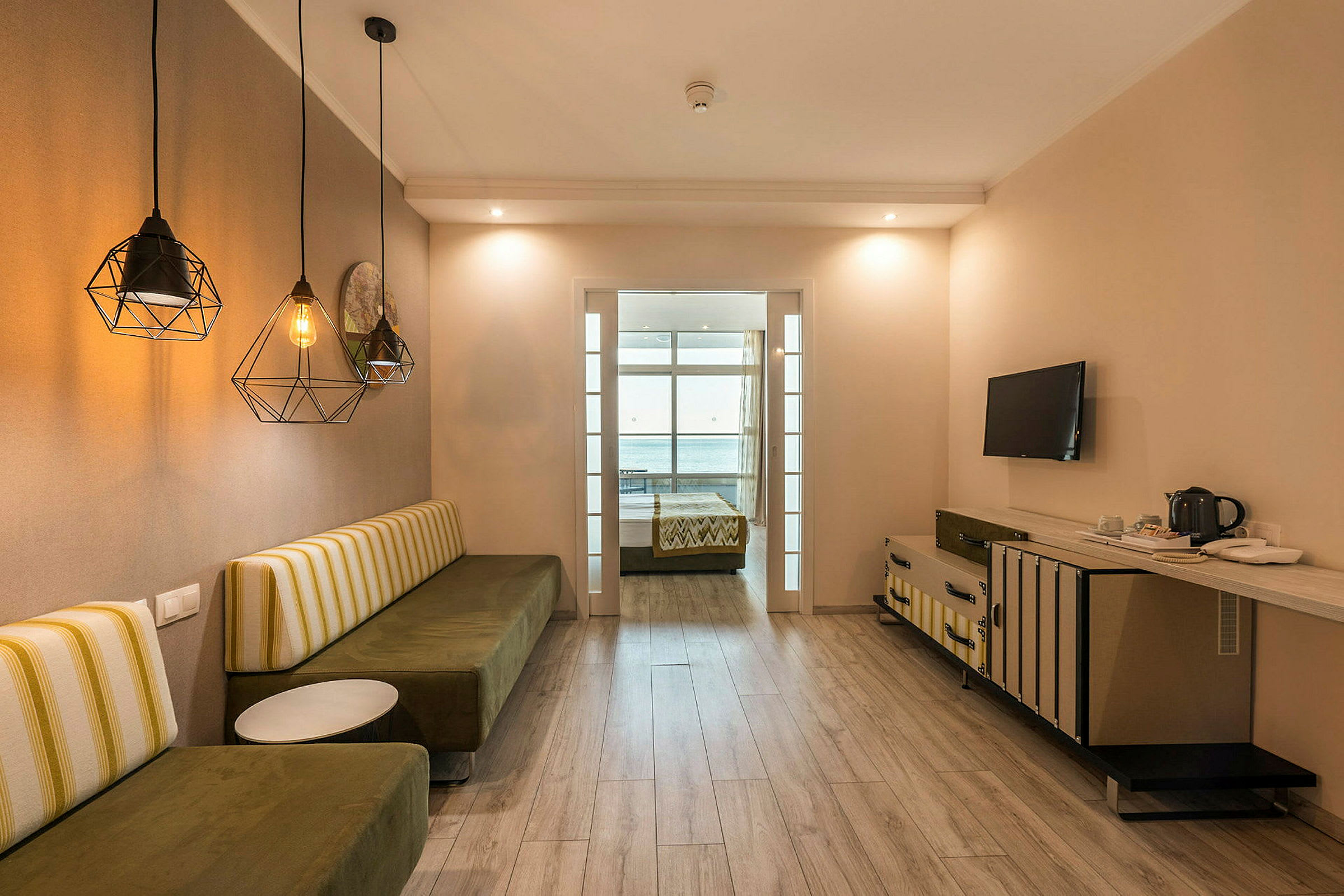 Ett hotellrum med en sittbänk, bord, TV och en säng i bakgrunden. (AI-genererad text)