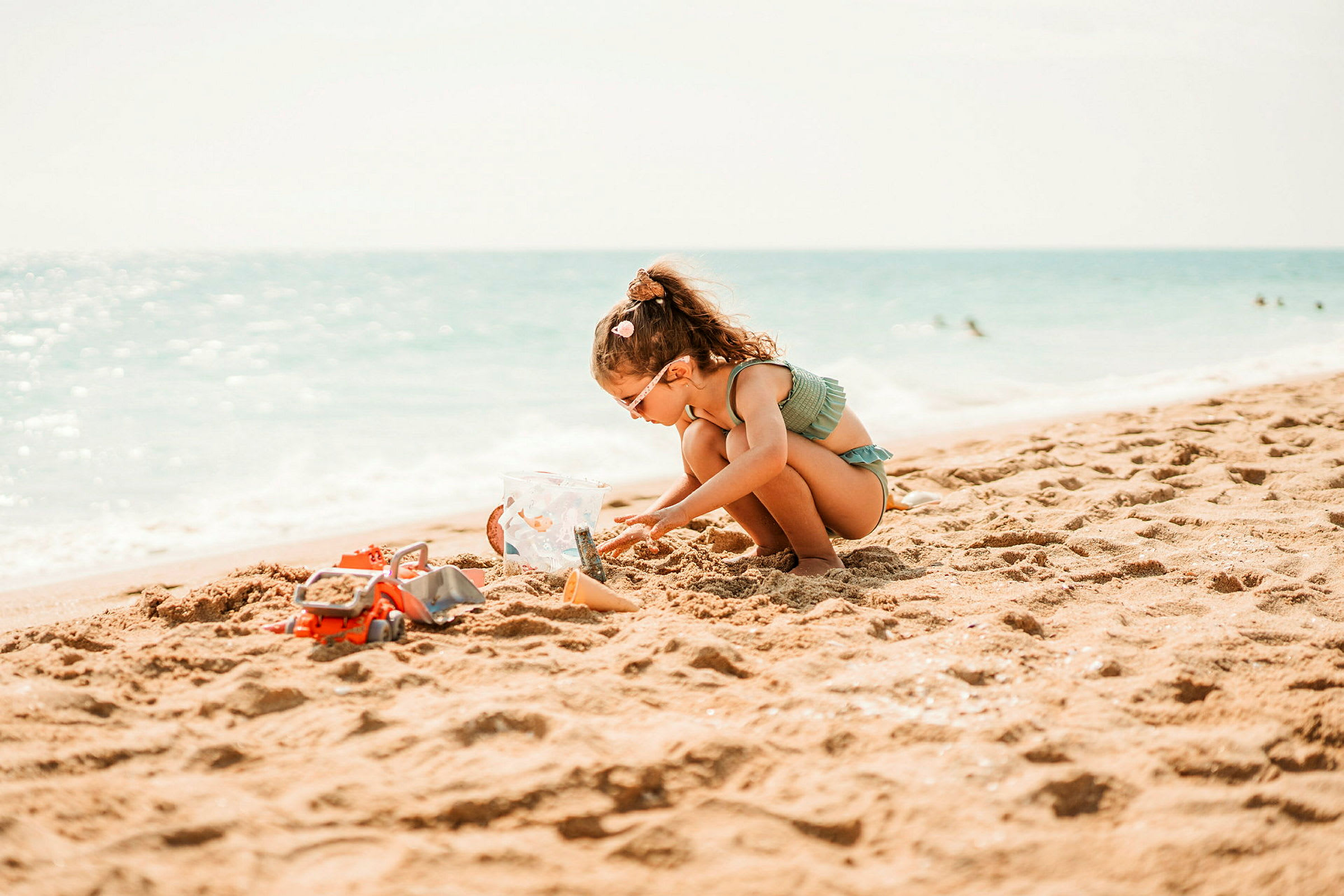 Ett barn leker med sand och leksaker på en solig strand nära havet. (AI-genererad text)