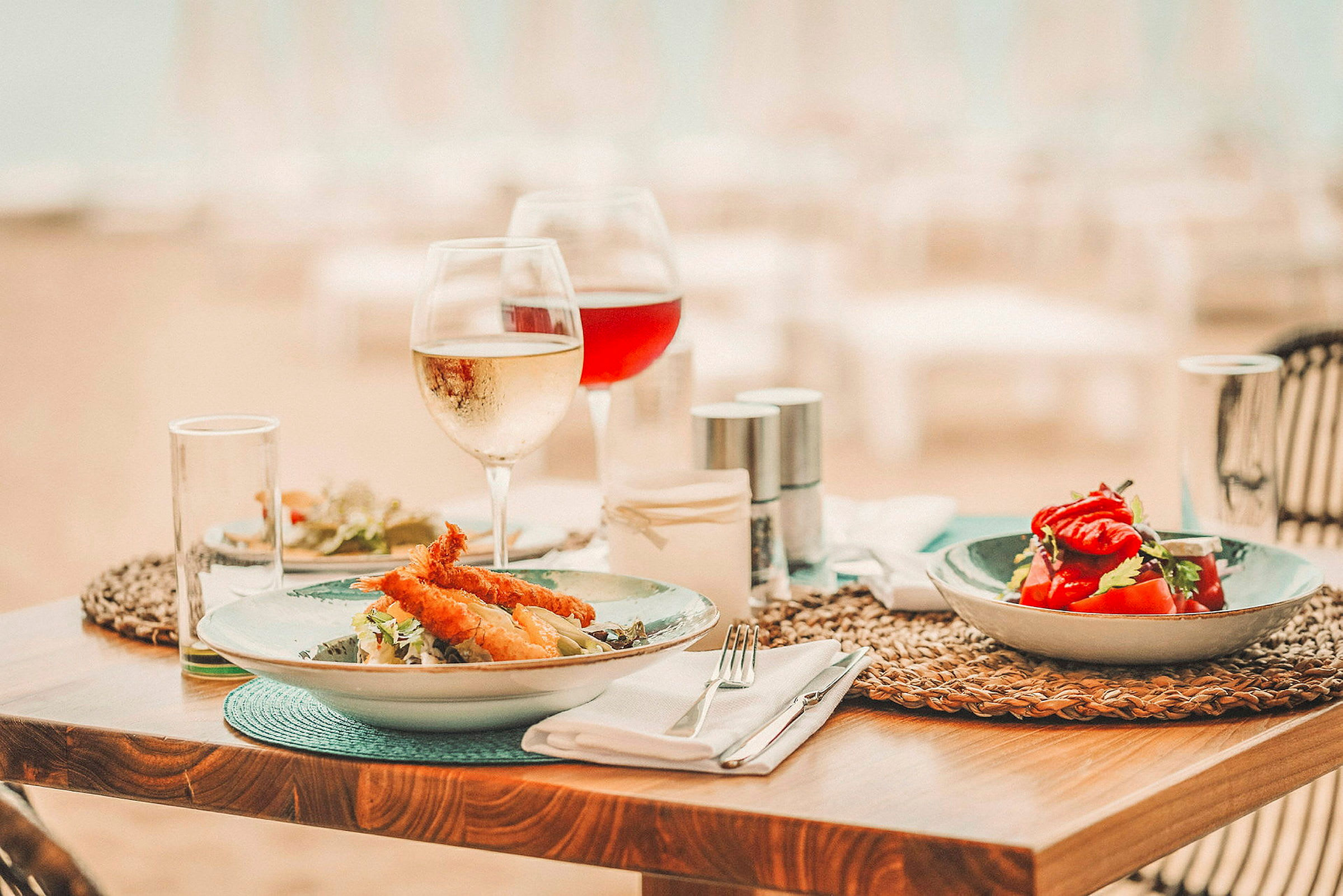 Matbord med tallrikar innehållande sallad och friterad mat, tillsammans med vinglas. (AI-genererad text)