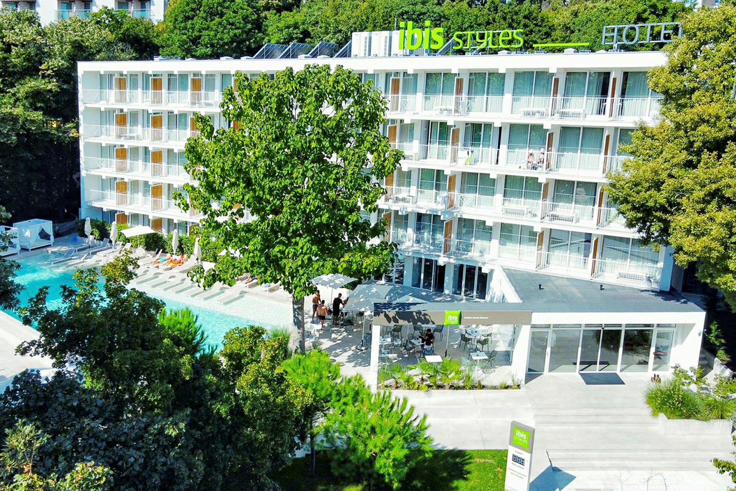 Hotellbyggnad med balkonger framför en swimmingpool, omgiven av träd. (AI-genererad text)