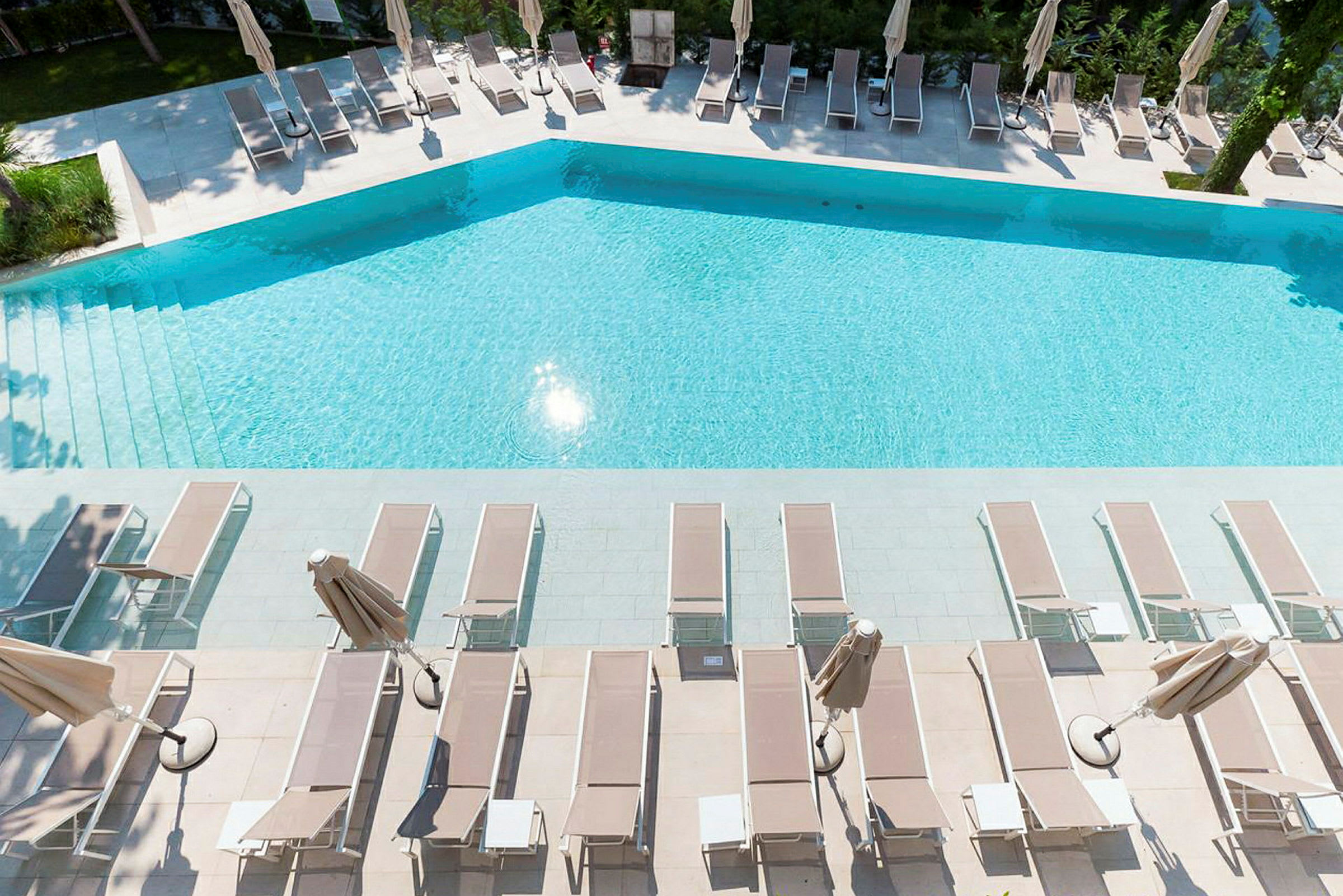 En swimmingpool med solstolar och parasoller vid sidan. (AI-genererad text)