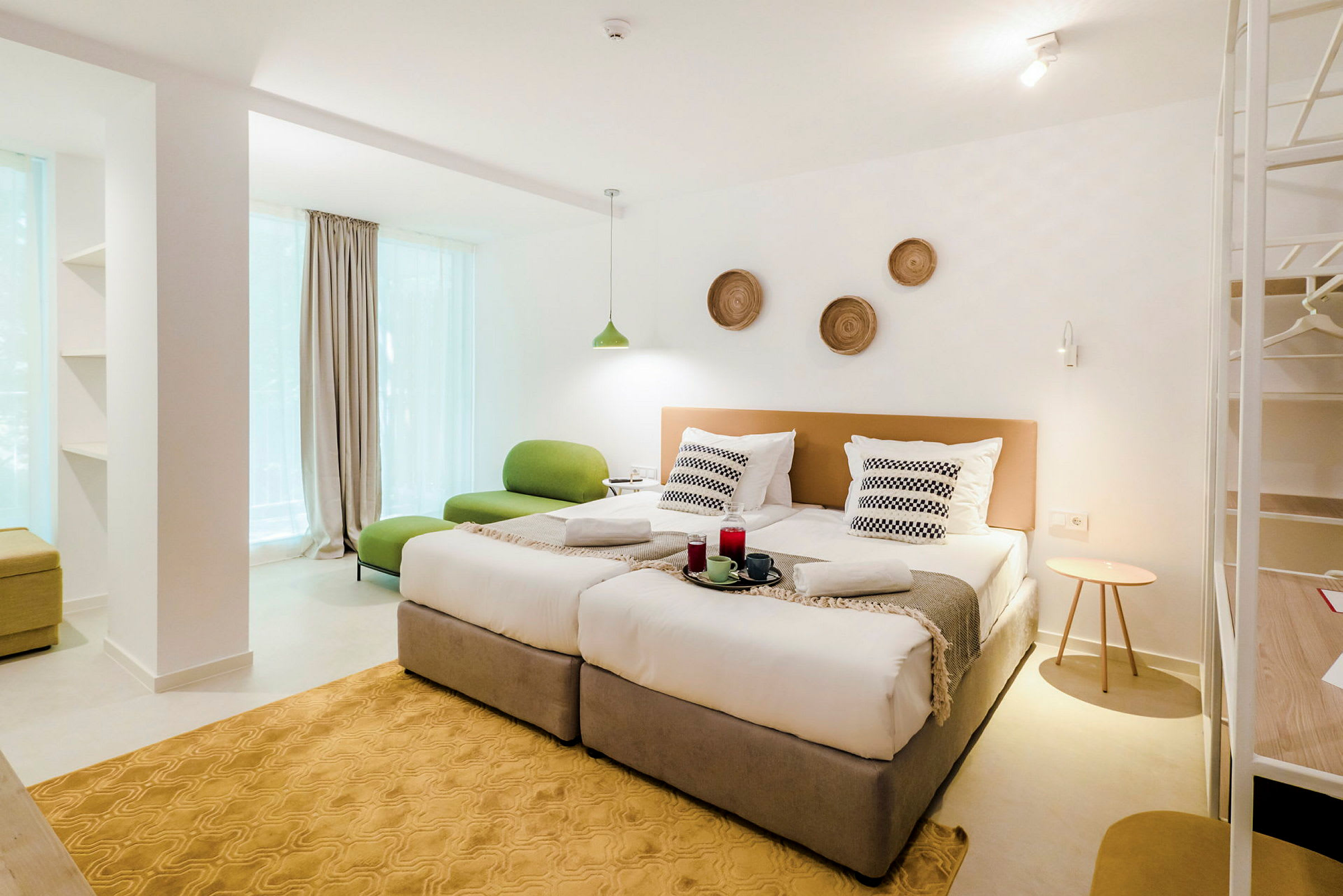 Ett modernt hotellrum med två enkelsängar, grön sittmöbel och dekorationer på väggen. (AI-genererad text)