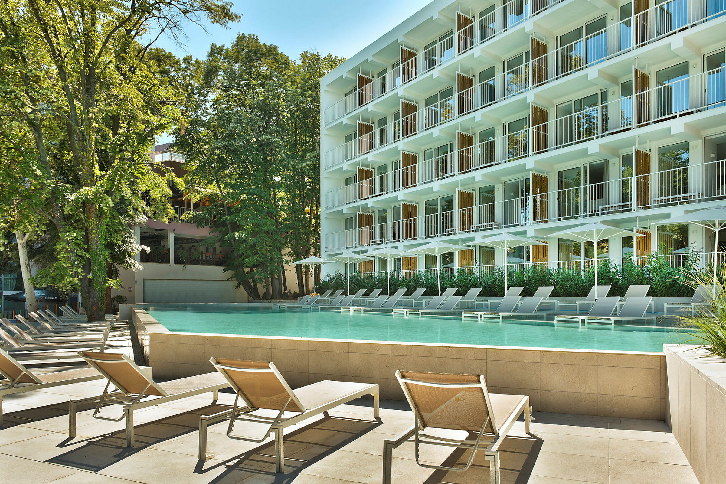 Hotellbyggnad med balkonger och en pool omgiven av solstolar. (AI-genererad text)