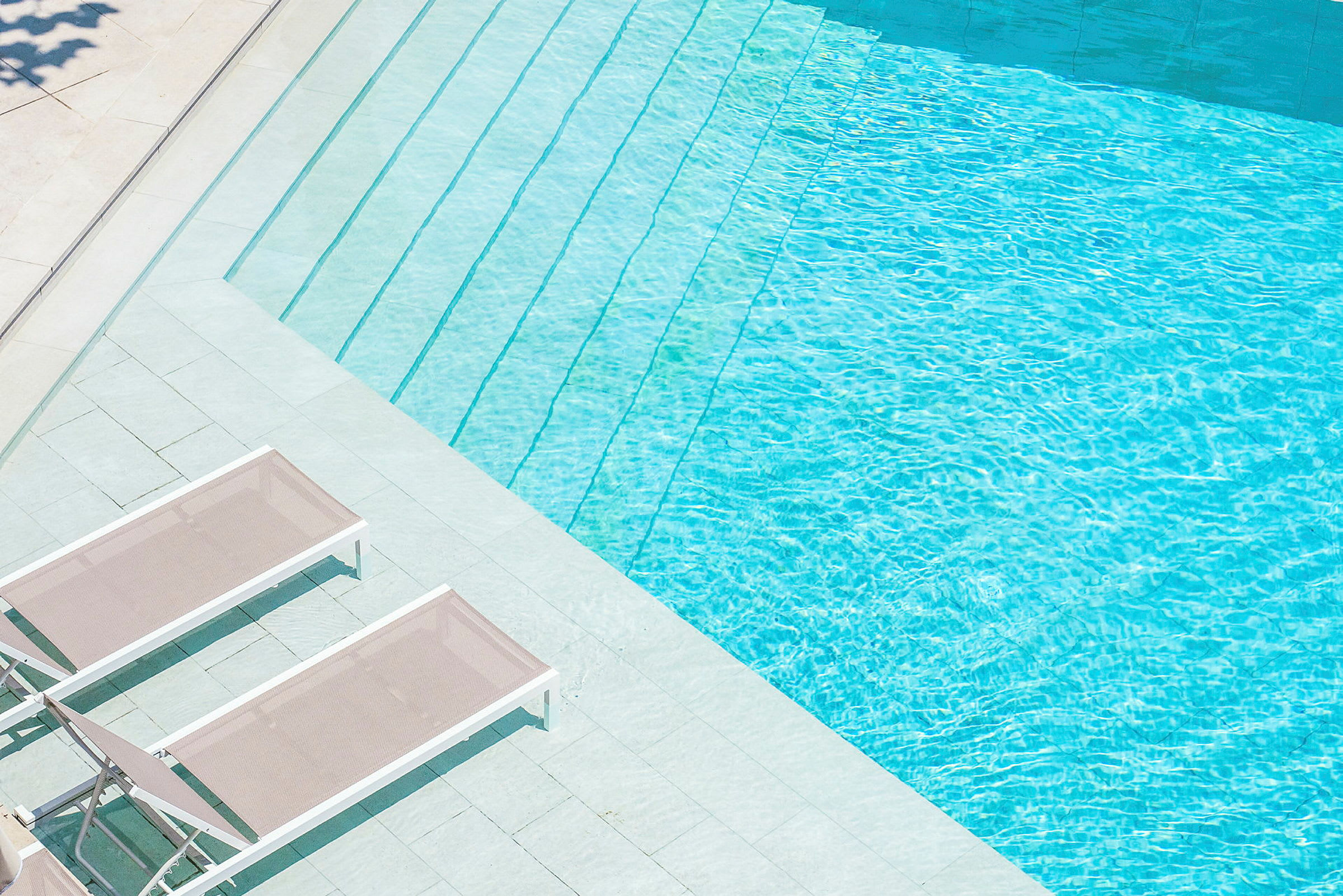 Ljusa solstolar bredvid en klarblå pool. (AI-genererad text)